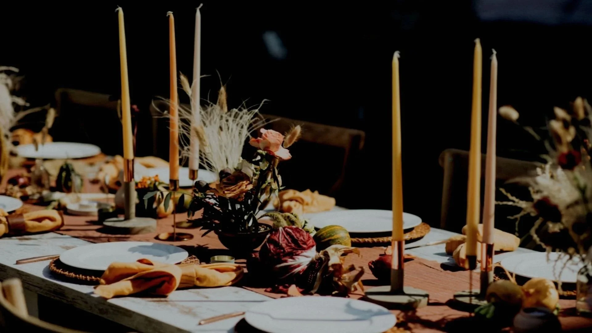 Decorated dining table with candles, flowers, gourds, and autumn-themed decorations in warm, earthy tones.