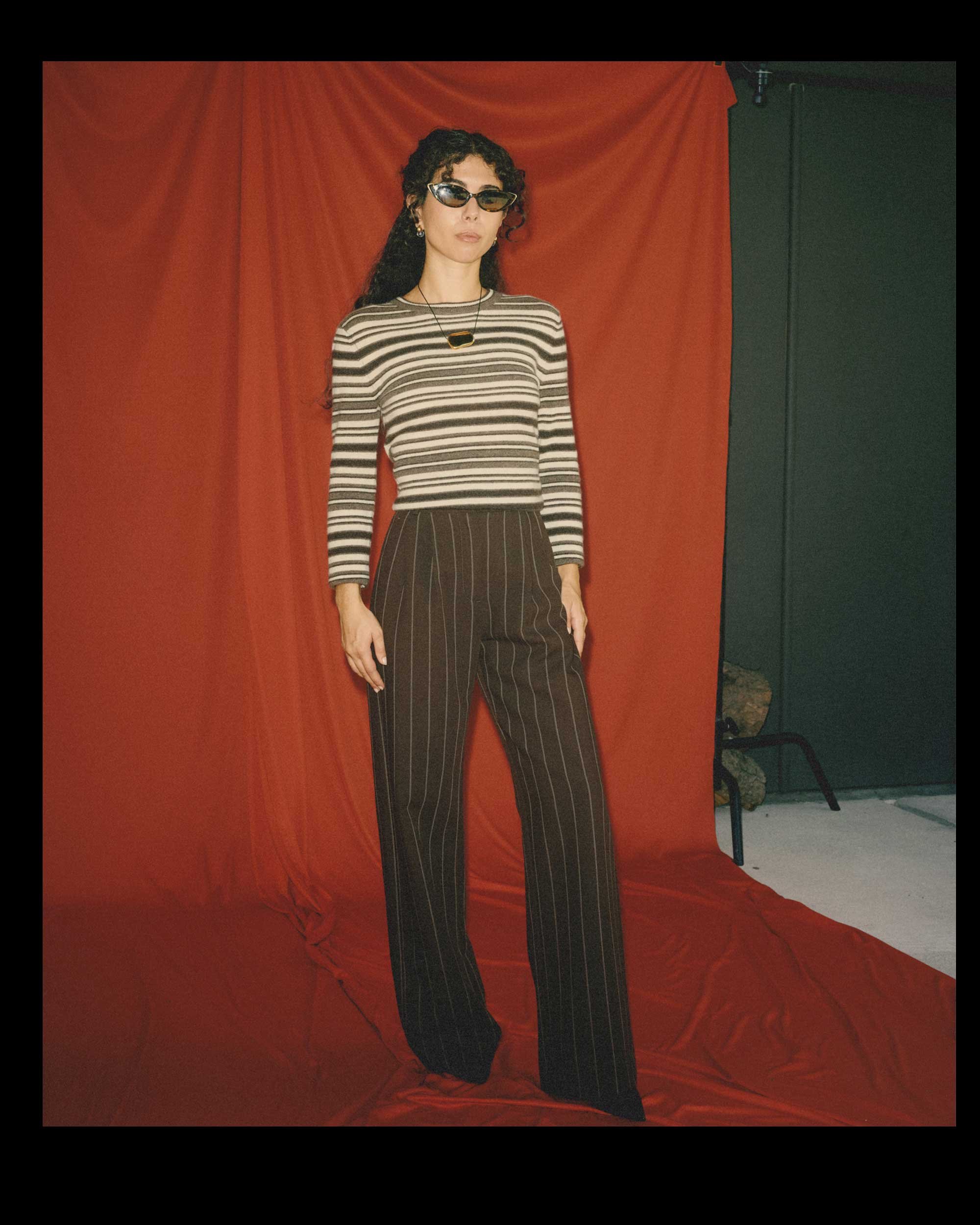 A short woman with a proportionally long torso and short legs pairs a horizontally striped sweater with high-rise, full-length brown pinstripe pants.