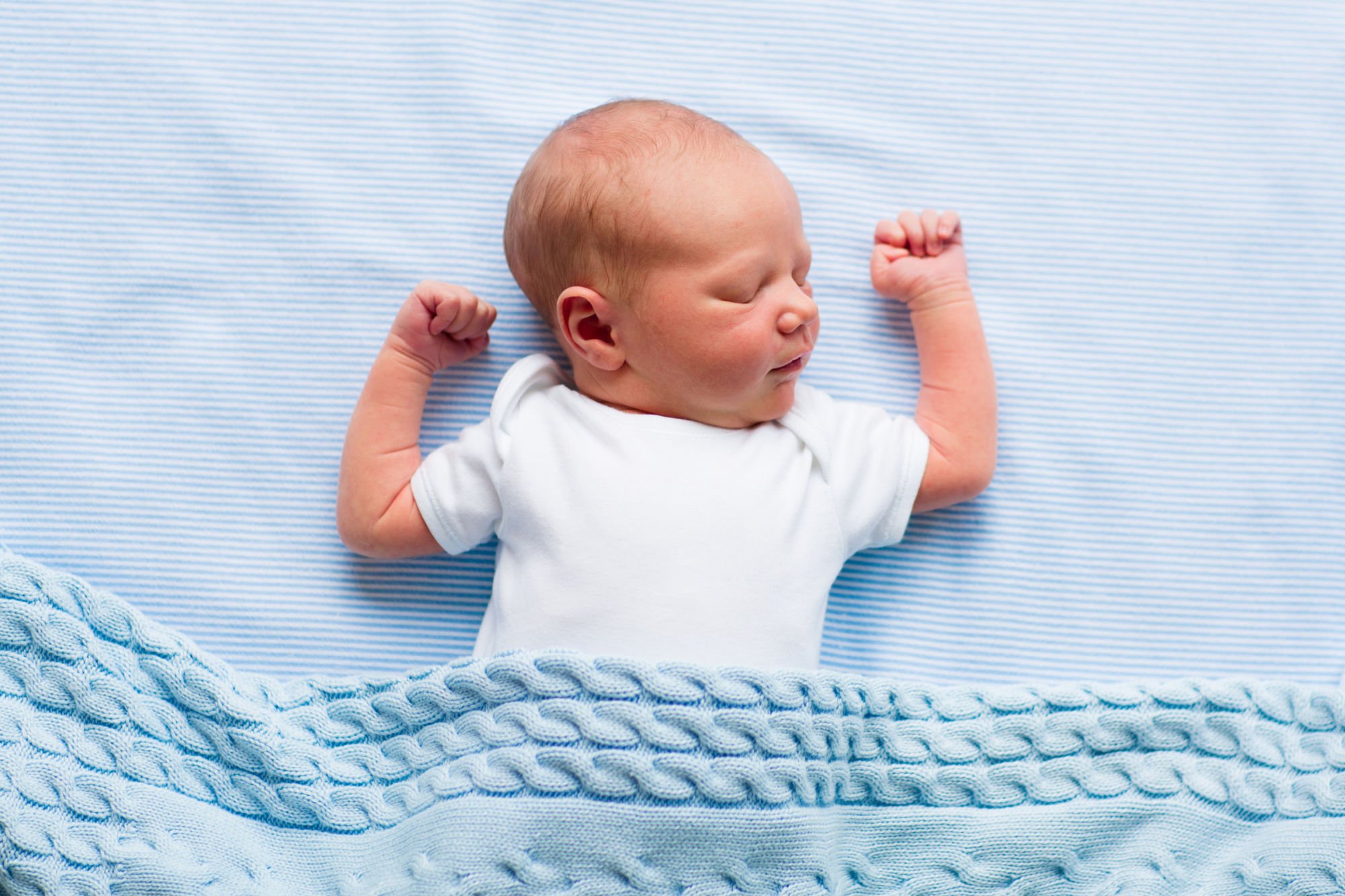 Sleeping baby on blue sheet with white onesie covered by blue knitted blanket_PBB.jpg