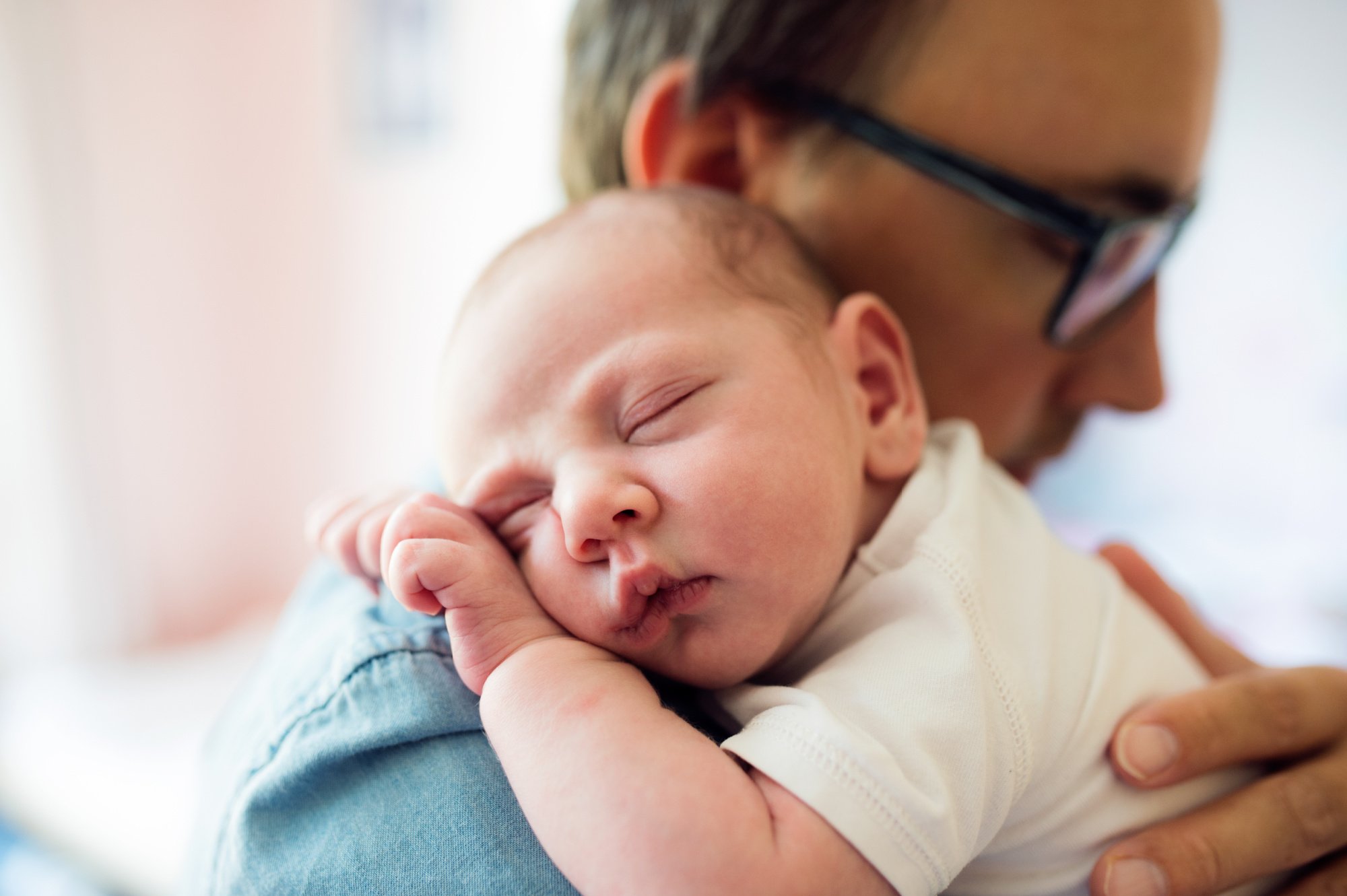 Baby sleeping wearing white being held by Dad wearing blue shirt and glasses_PBB.jpg