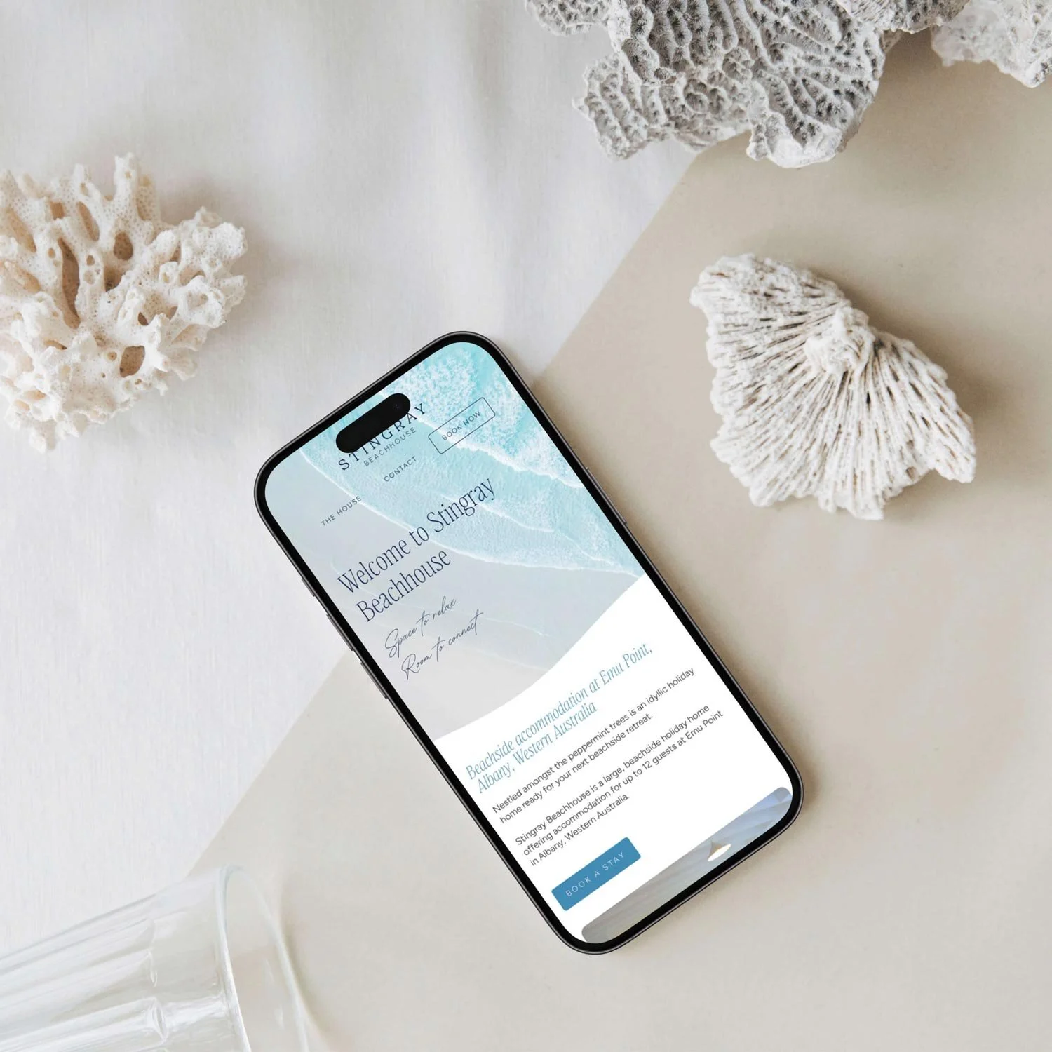Stingray Beachhouse website shown on iPhone surrounded by shells and coral, designed by Queensland sustainable WordPress website designer, Whale Tail Digital