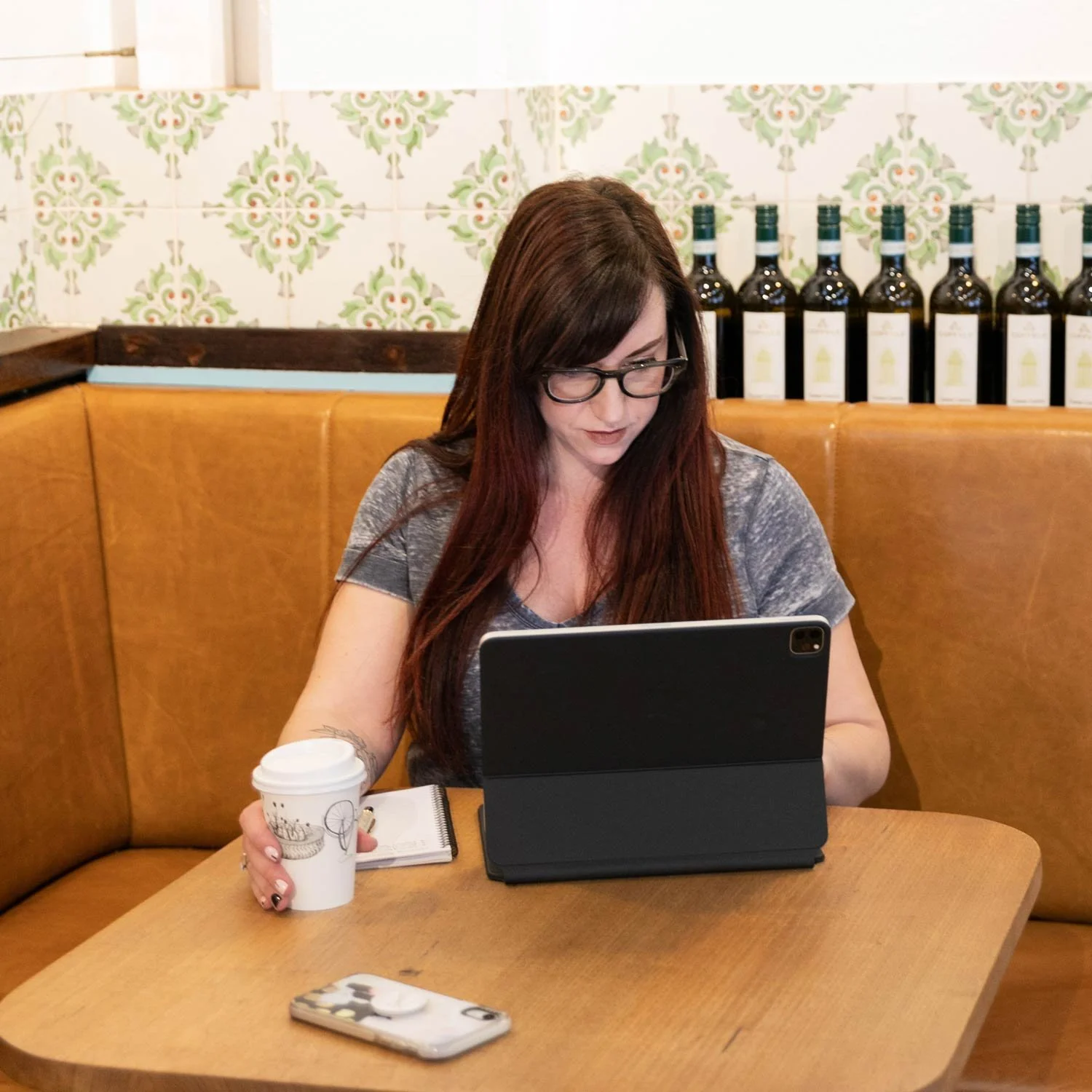 Joanne Tapodi, Perth logo & website designer, and founder of Creativault sitting in a cafe with coffee & iPad