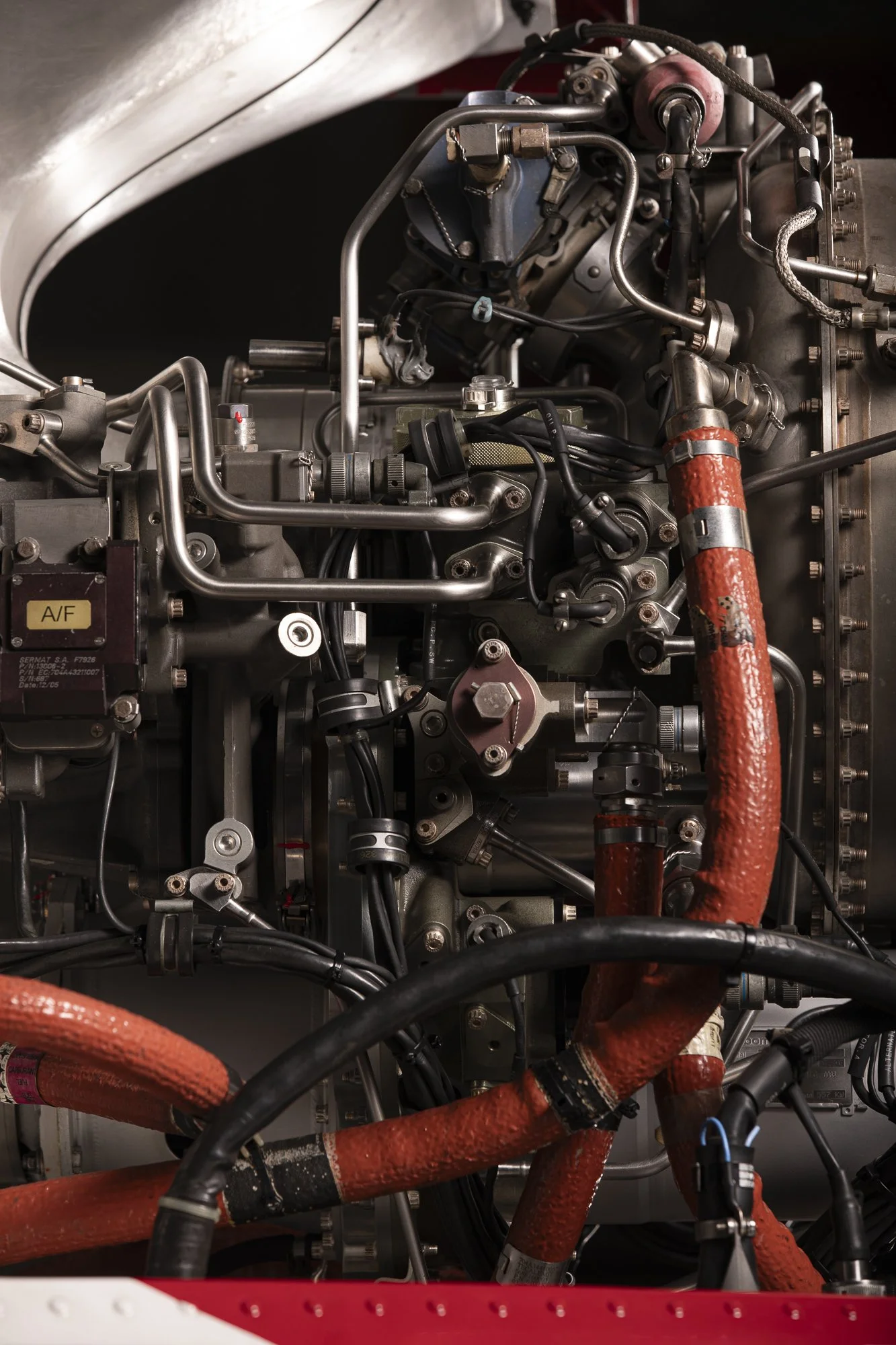 Moteur d'avion avec tubes et câbles métalliques, certains isolés avec du ruban adhésif orange.