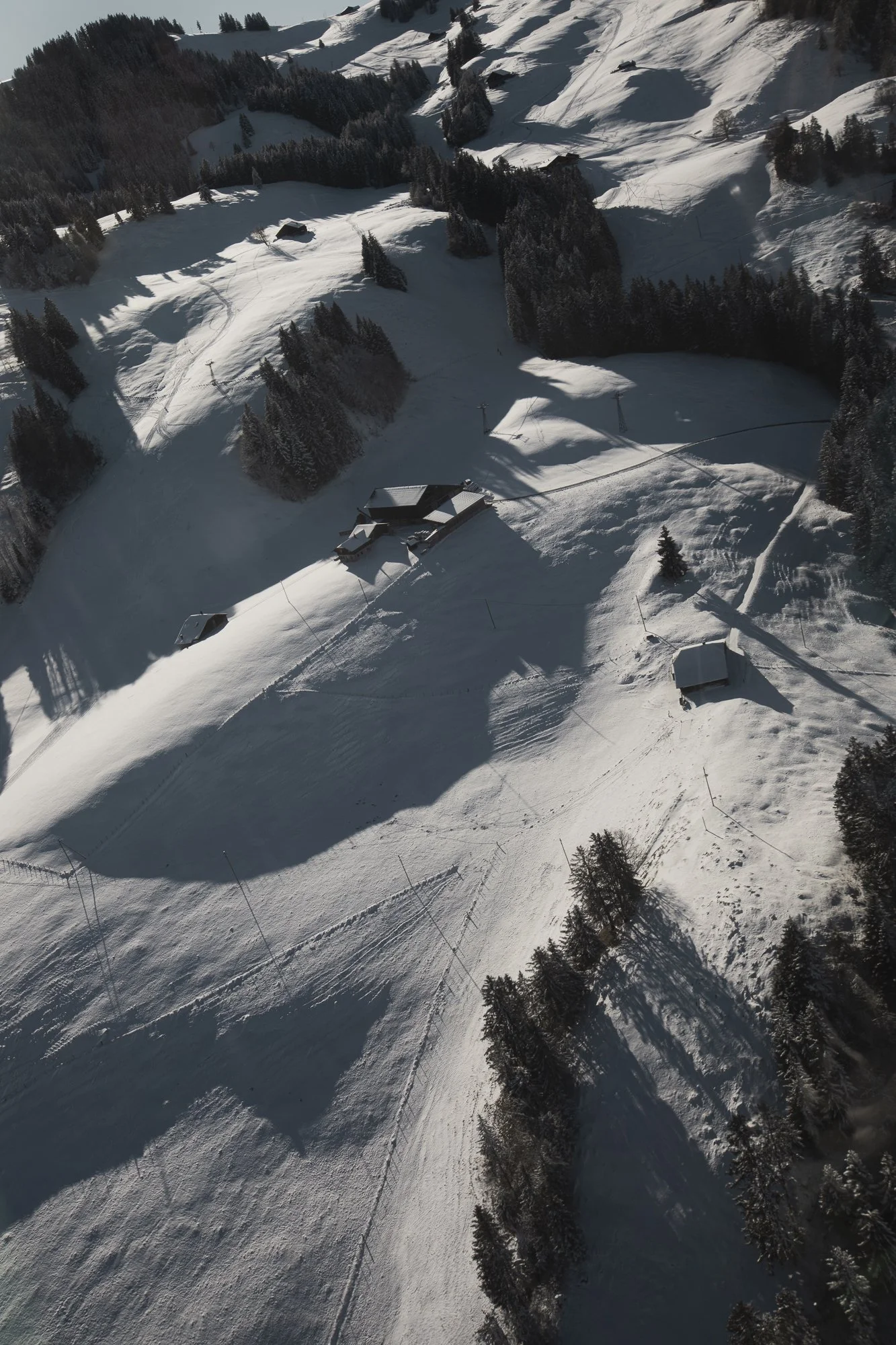 Paysage hivernal avec des collines enneigées, des arbres et quelques bâtiments isolés.