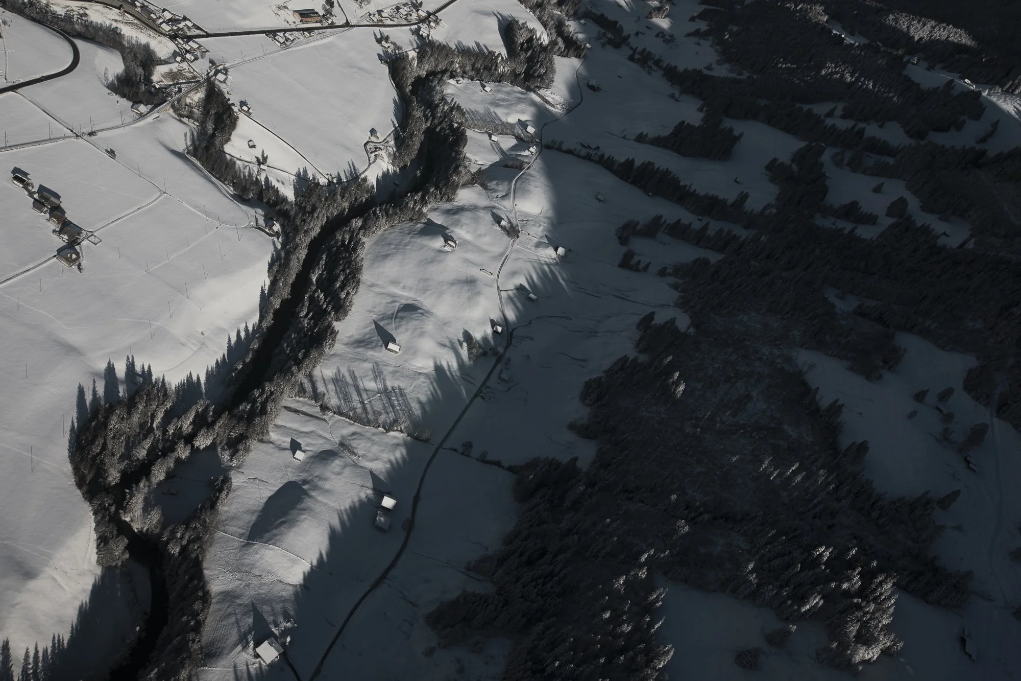Paysage enneigé avec des forêts, des routes étroites et quelques bâtiments dans une région montagneuse.