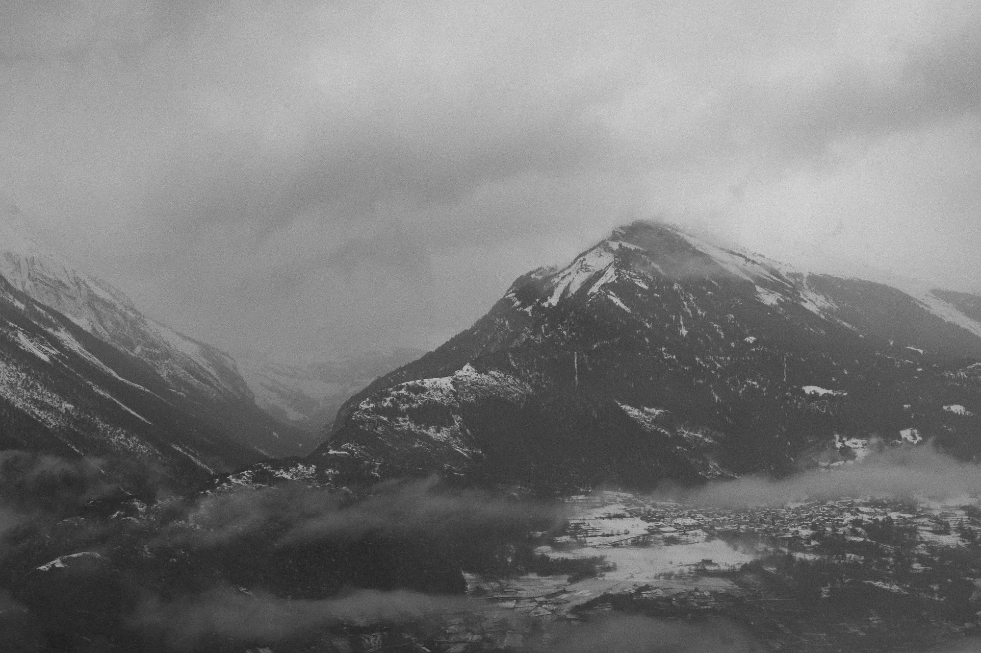Montagne enneigée avec des nuages sombres et brouillard dans une vallée enneigée.