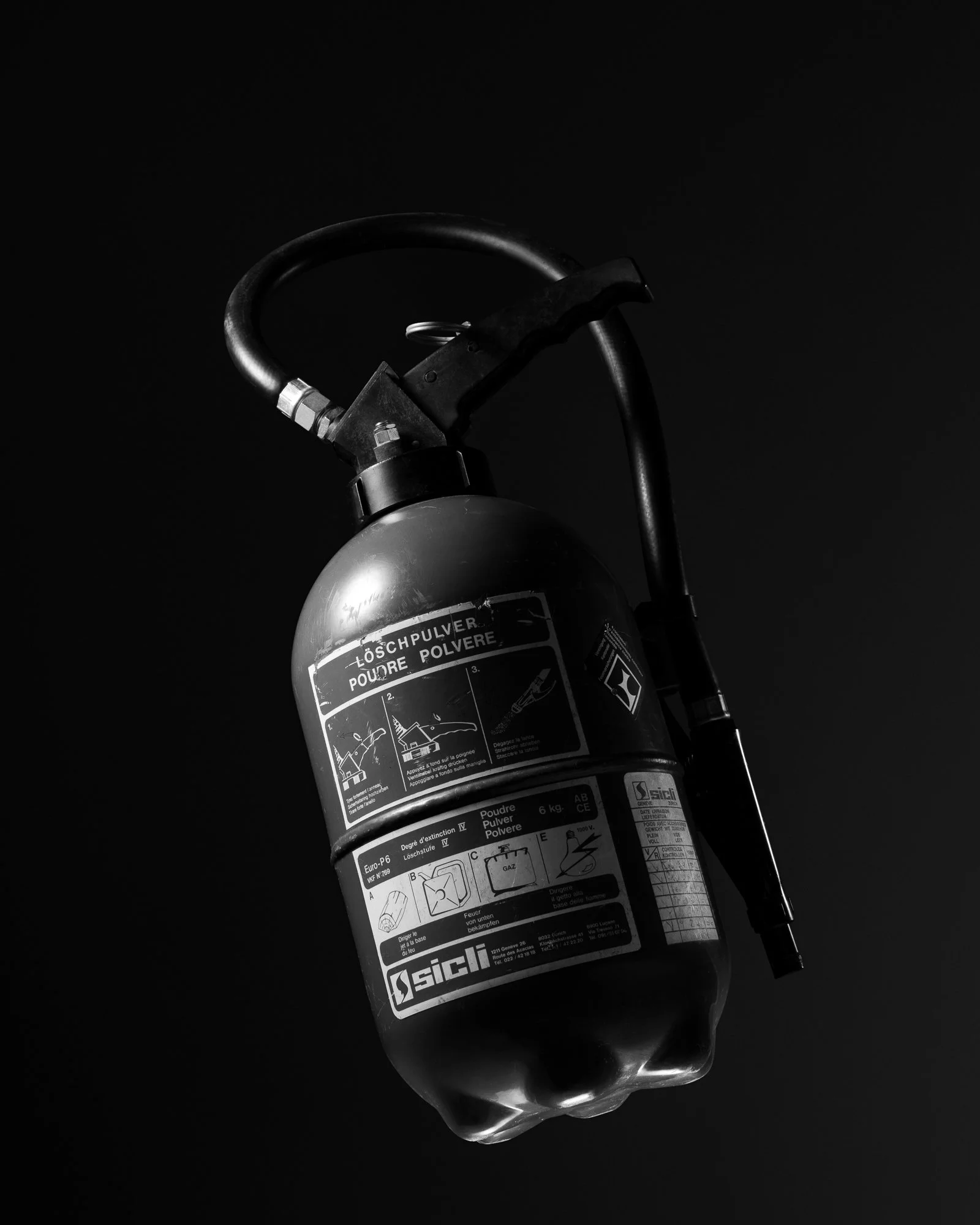 Extincteur à poudre noir avec étiquettes en français, placé dans un fond noir.