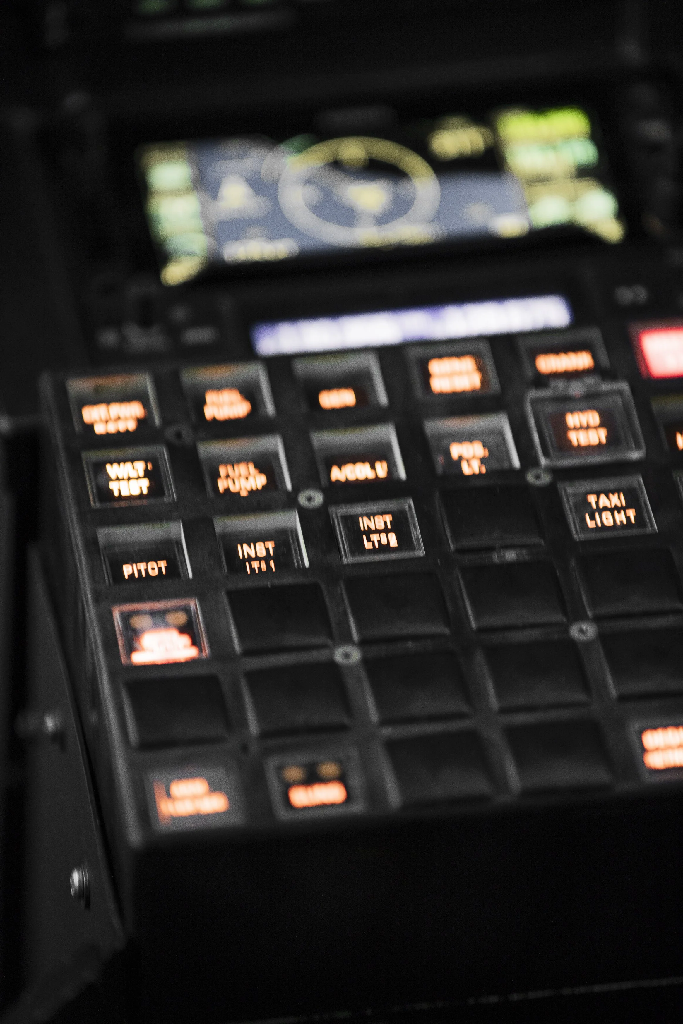 Tableau de commandes d'un cockpit d'avion avec plusieurs boutons lumineux, en partie flous.