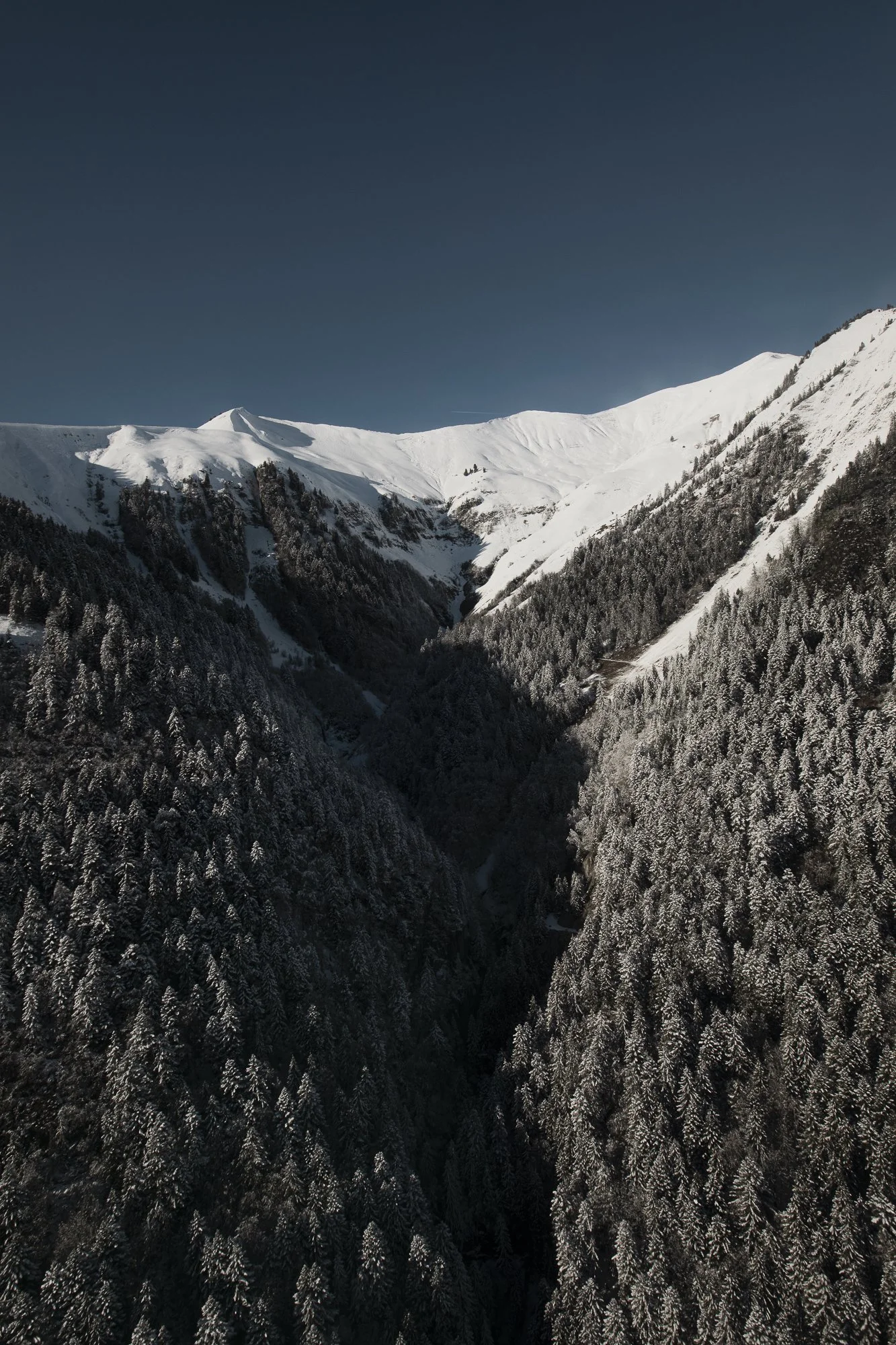 Vallée de montagnes enneigées avec sommet au loin sous un ciel bleu.