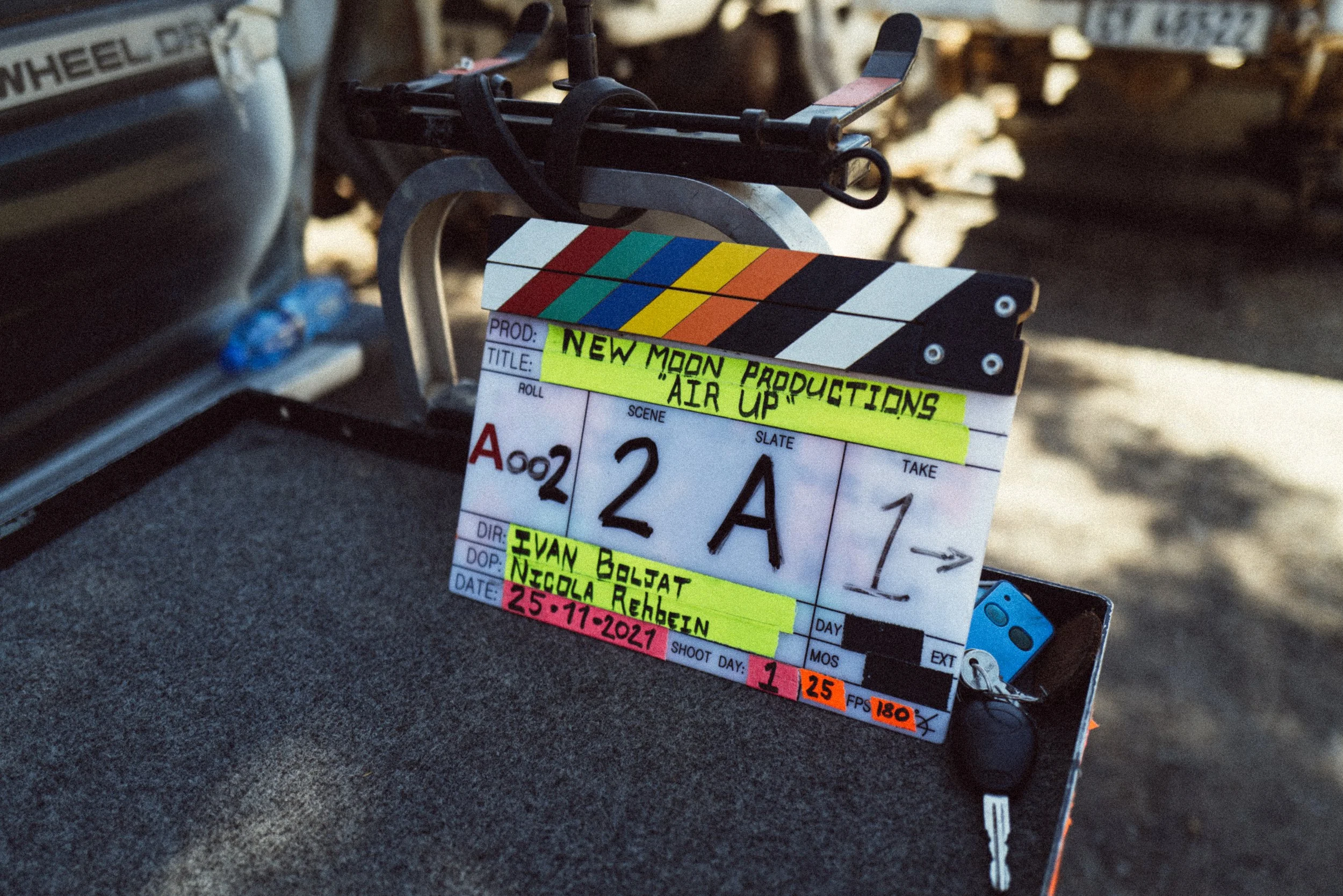 A film clapperboard with colorful top stripes, labeled "New Moon Productions - Air Up," showing scene 2A take 1. There are keys and a device next to it on a cart.