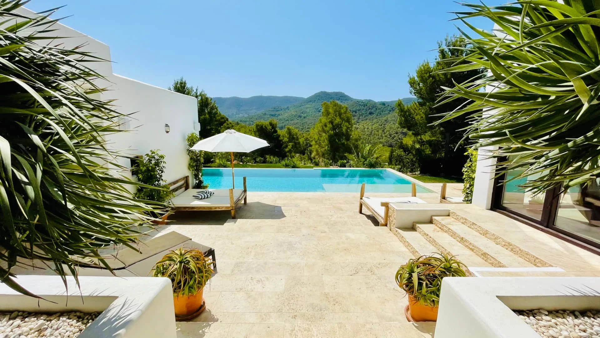 Luxury backyard with swimming pool, outdoor lounge chairs, potted plants, and mountain view under a clear blue sky.