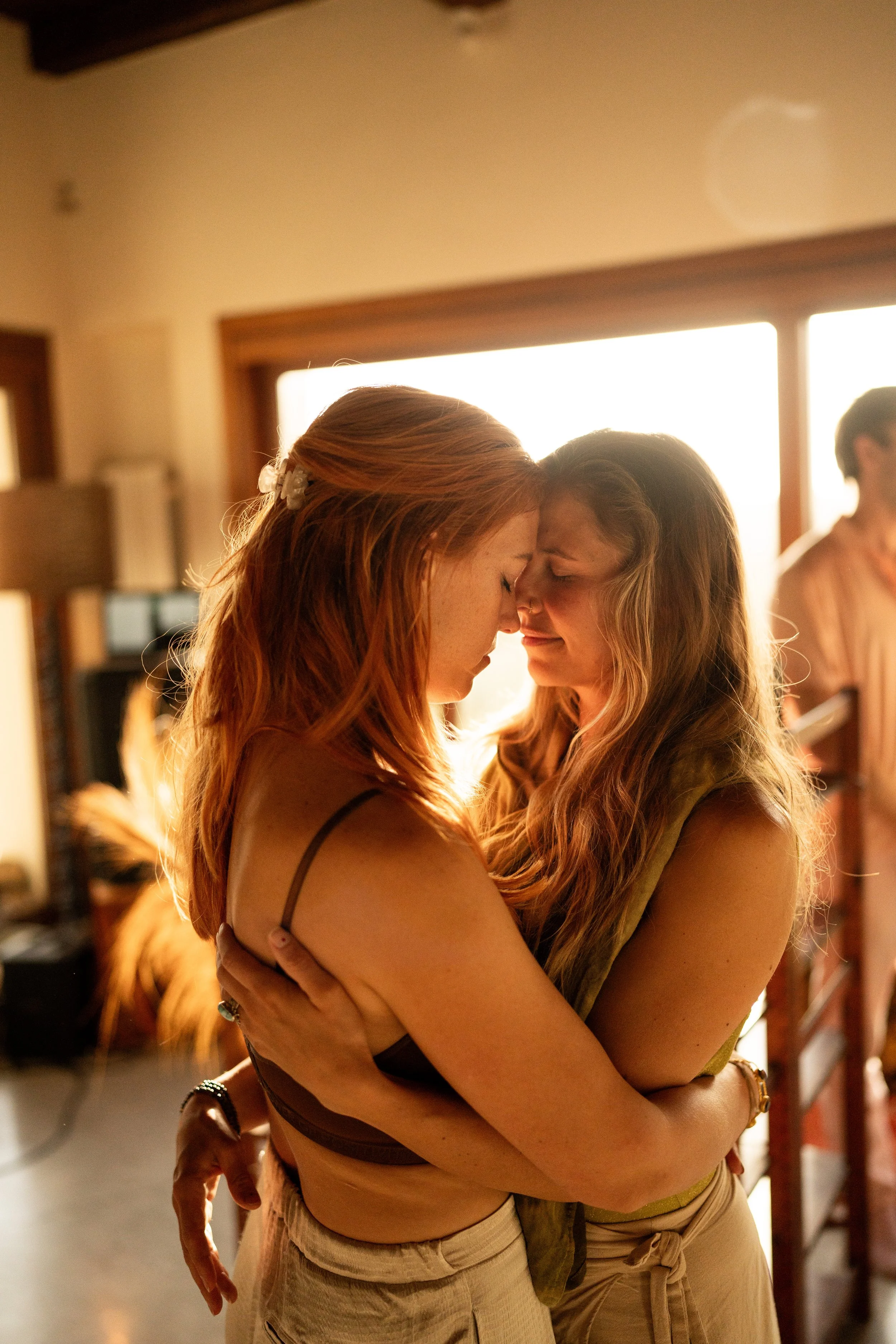 Two women hugging each other with foreheads touching in a warmly lit room.