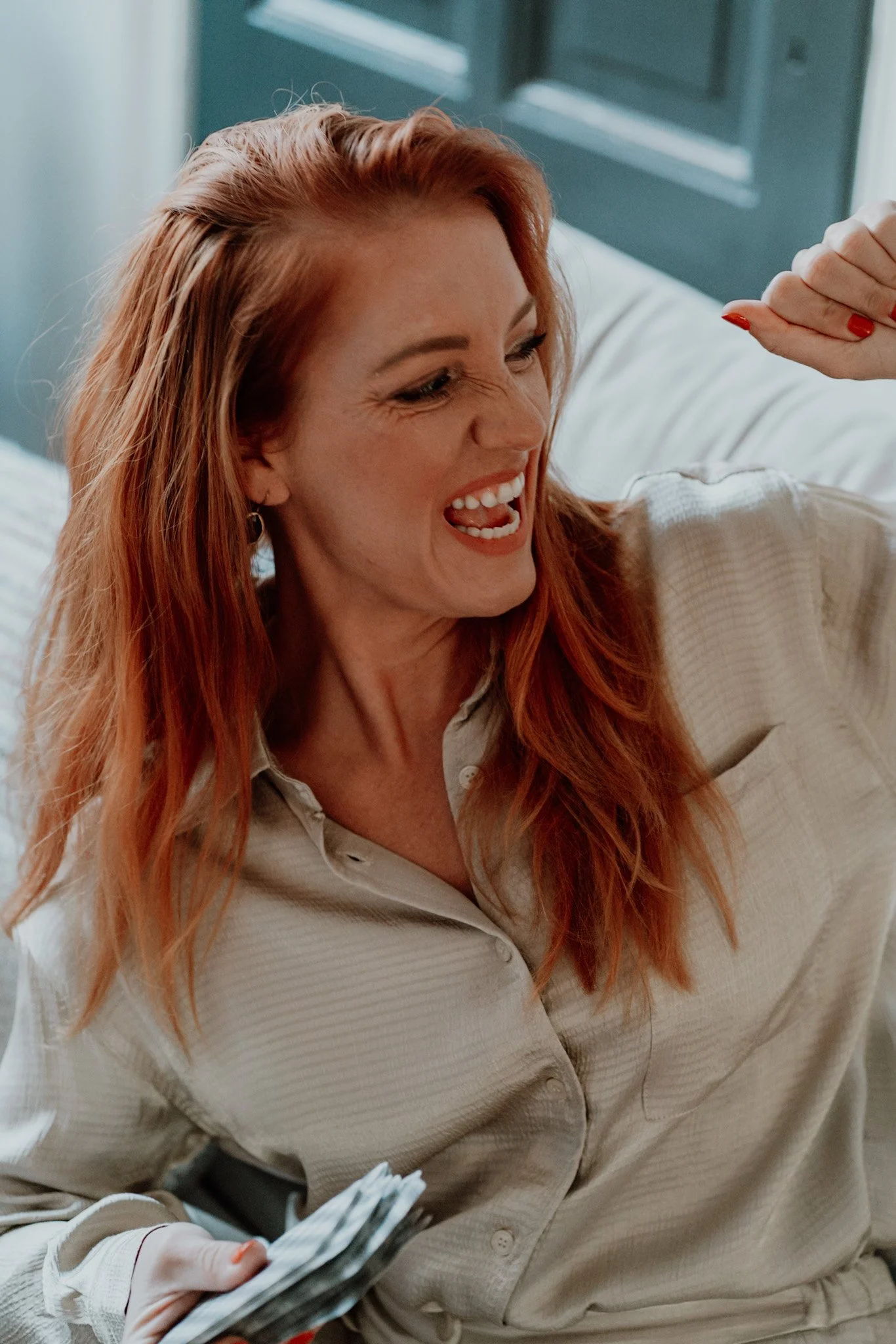 A woman with red hair and a beige shirt smiling and flexing her arm, holding a stack of money.