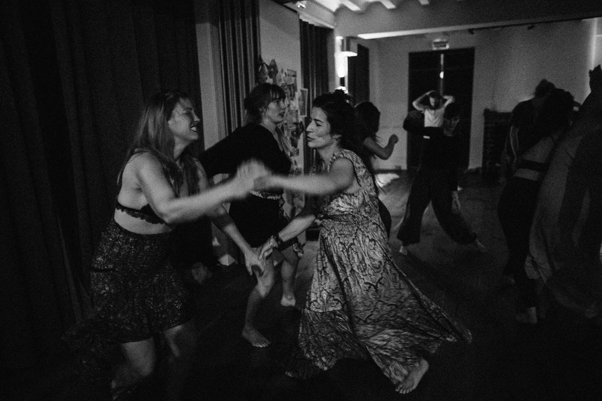 People dancing at a party, smiling and holding hands, with others dancing in the background in a dimly lit room. dancing dans en beweging lichaamswerk embodiment
