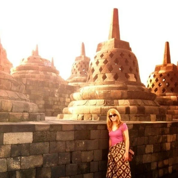 A woman with long hair and sunglasses standing next to historic stone stupas or pagodas at Borobudur Temple in Indonesia. travel ancient wisdom traditions karmayoga tantra thai medicine chines medicine bodyworker east meets west eastern rituals