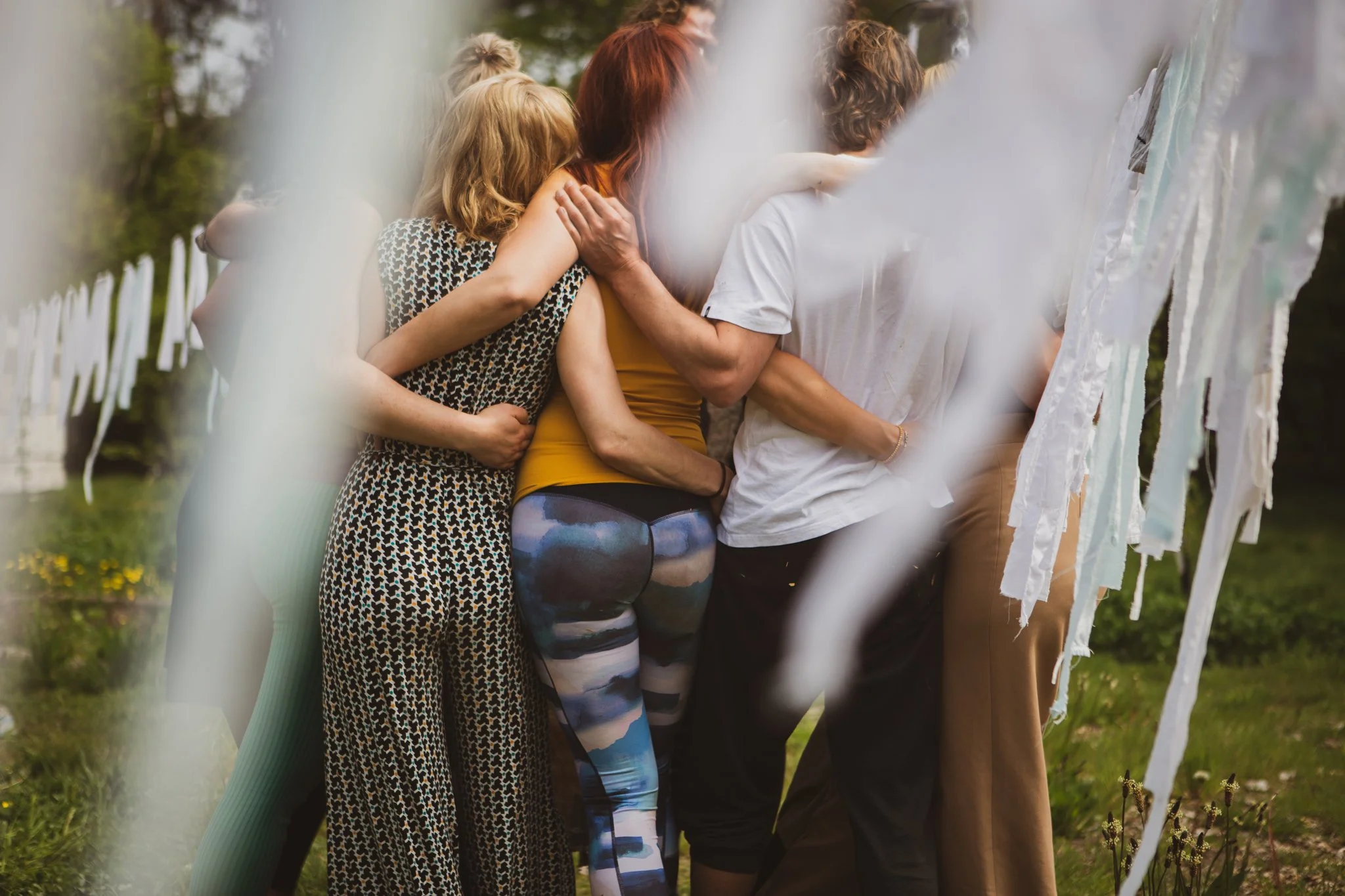Group of people hugging outdoors near hanging white fabric strips. grouphug cuddle puddle groepswerk lichaamscontact groepsknuffel aanraking regulation self regulation co regulation groupregulation tribal regulation tribe community