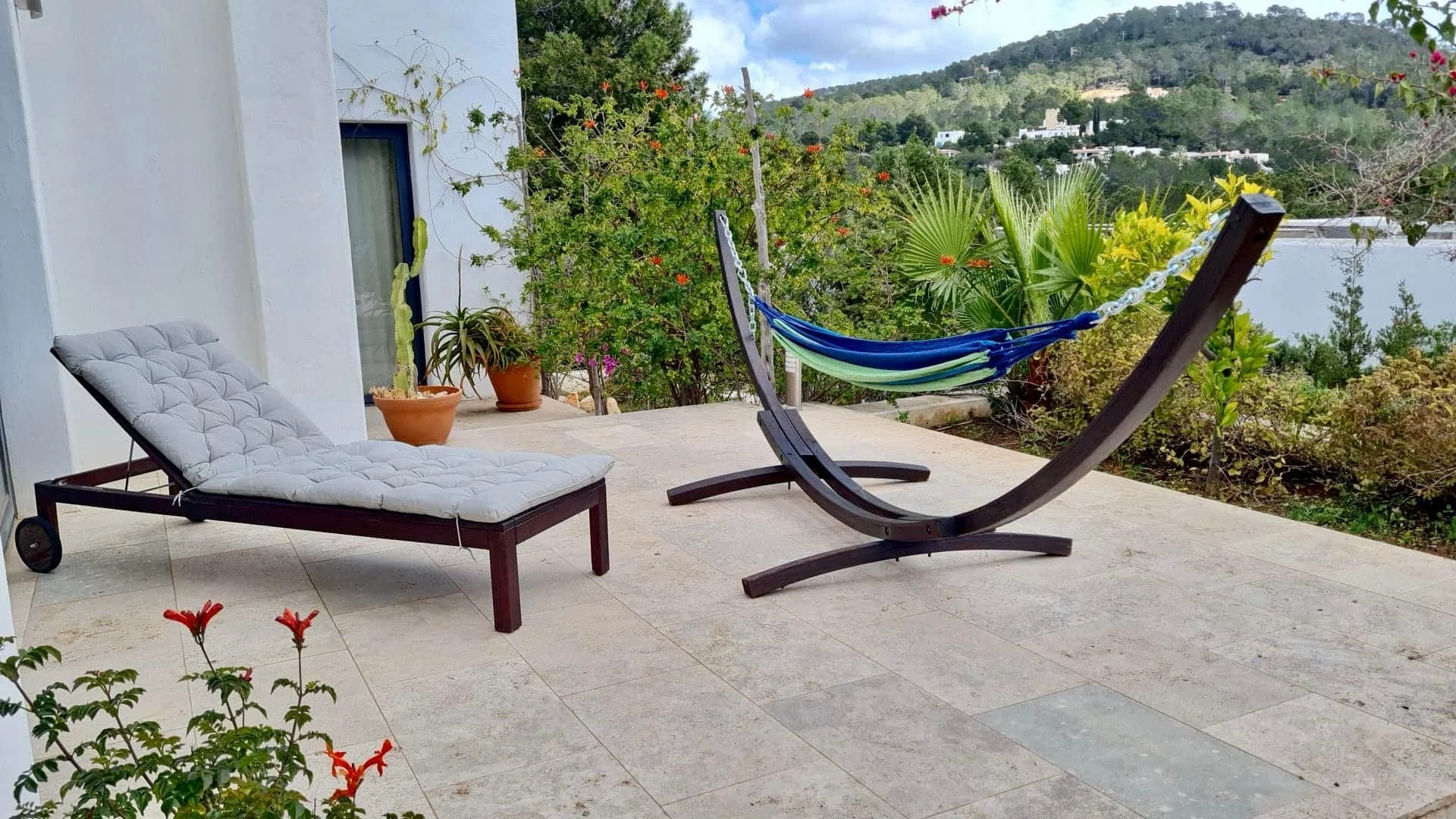 A patio with two lounge chairs, a hammock, potted plants, and scenic greenery in the background.