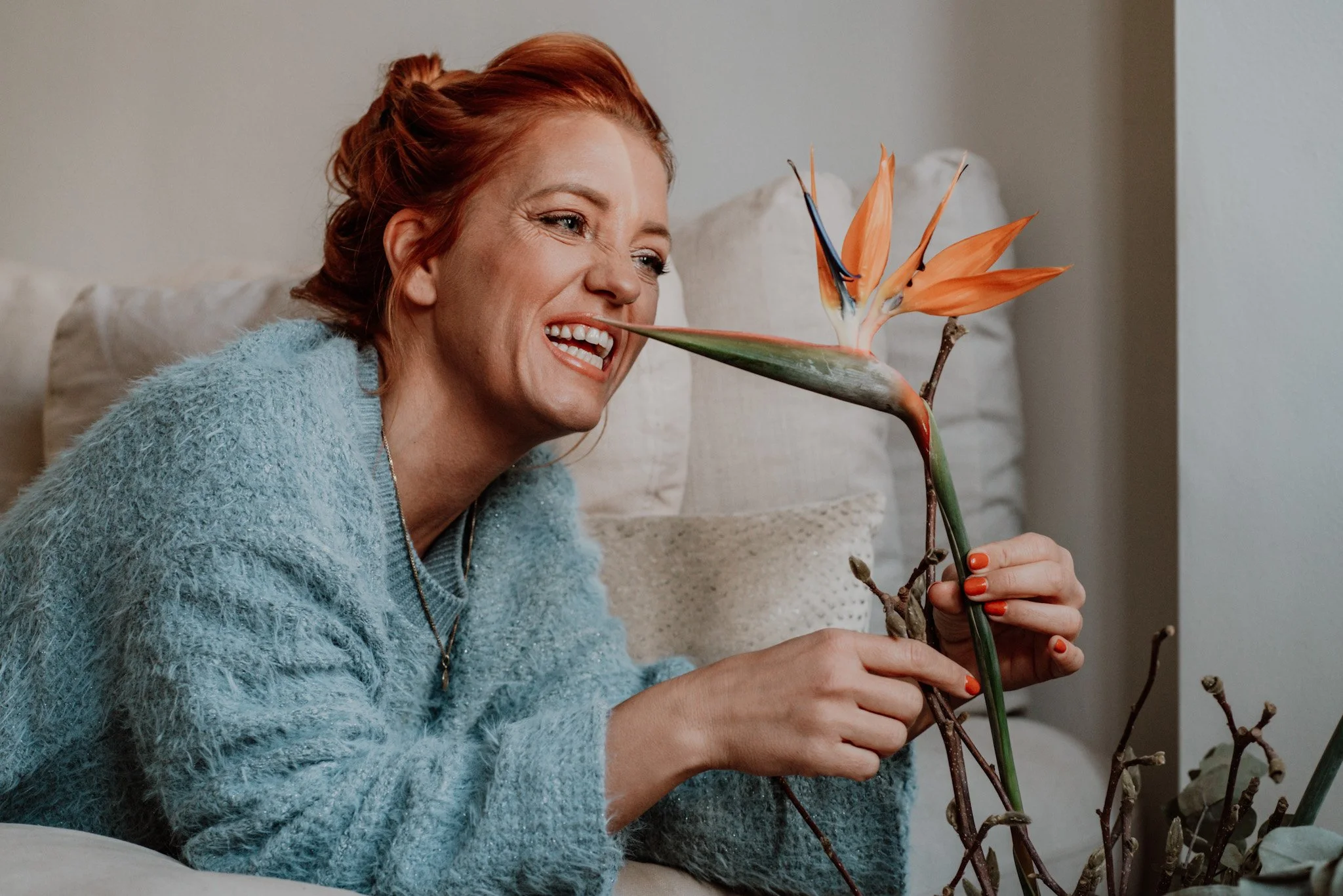 A woman with red hair smiling as she holds a bird of paradise flower.