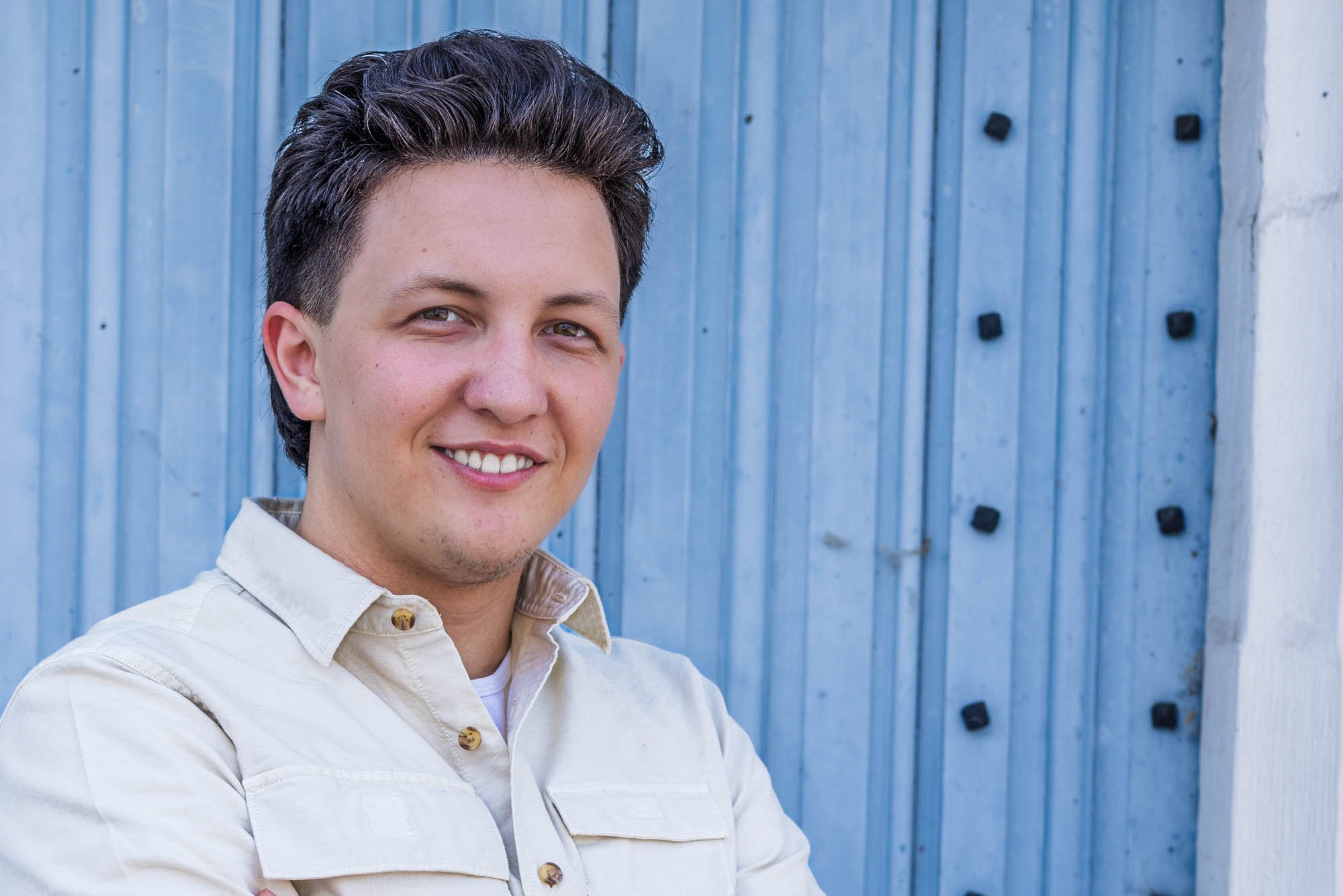 Portret van Alex Verspecht met blauwe achtergrond, lichtblauwe stalen deur als industriële setting in Mechelen"
