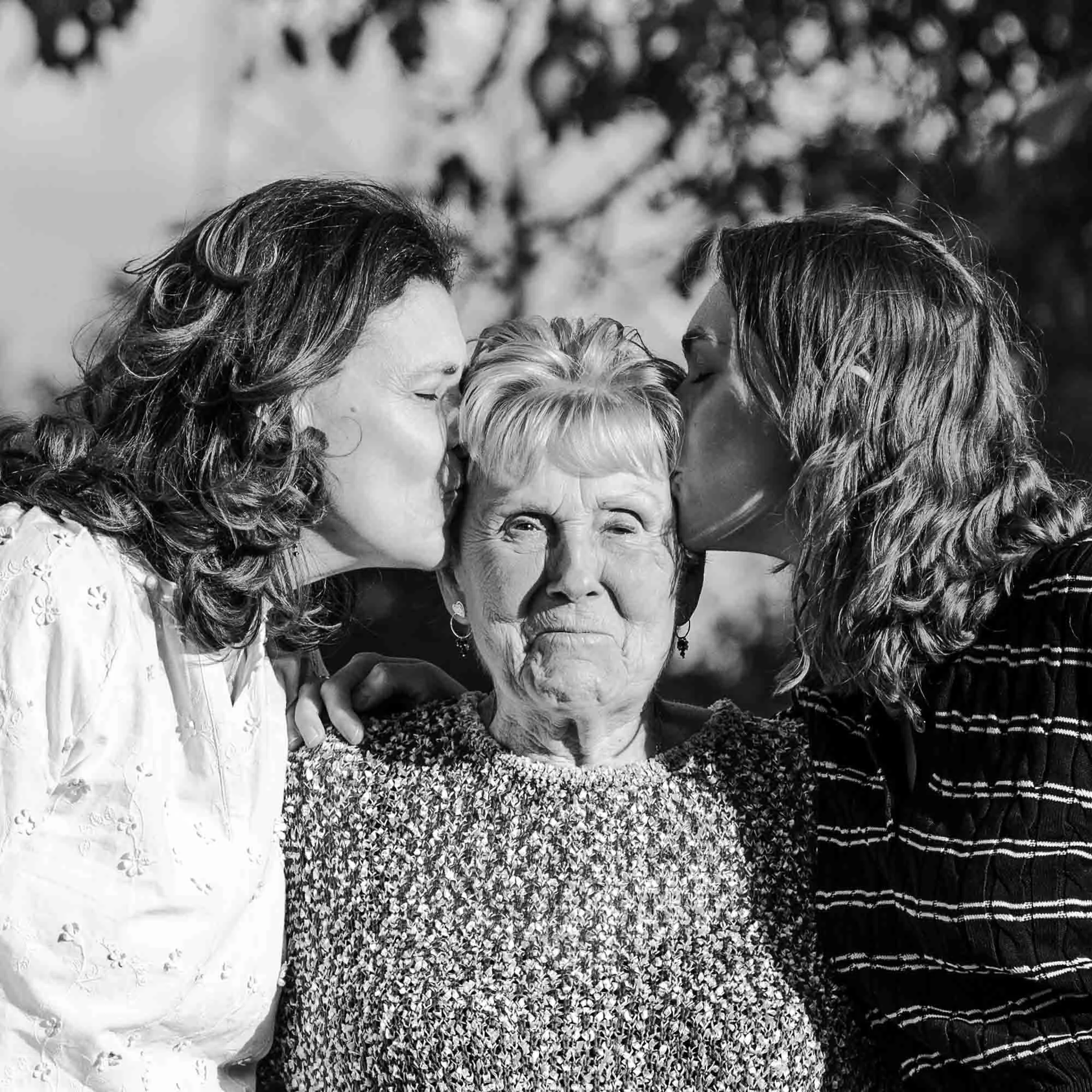 "Zwart-wit portret van Amber Sels en haar mama die haar grootmoeder elk een kus op het voorhoofd geven, intiem familiemoment in Rijmenam"