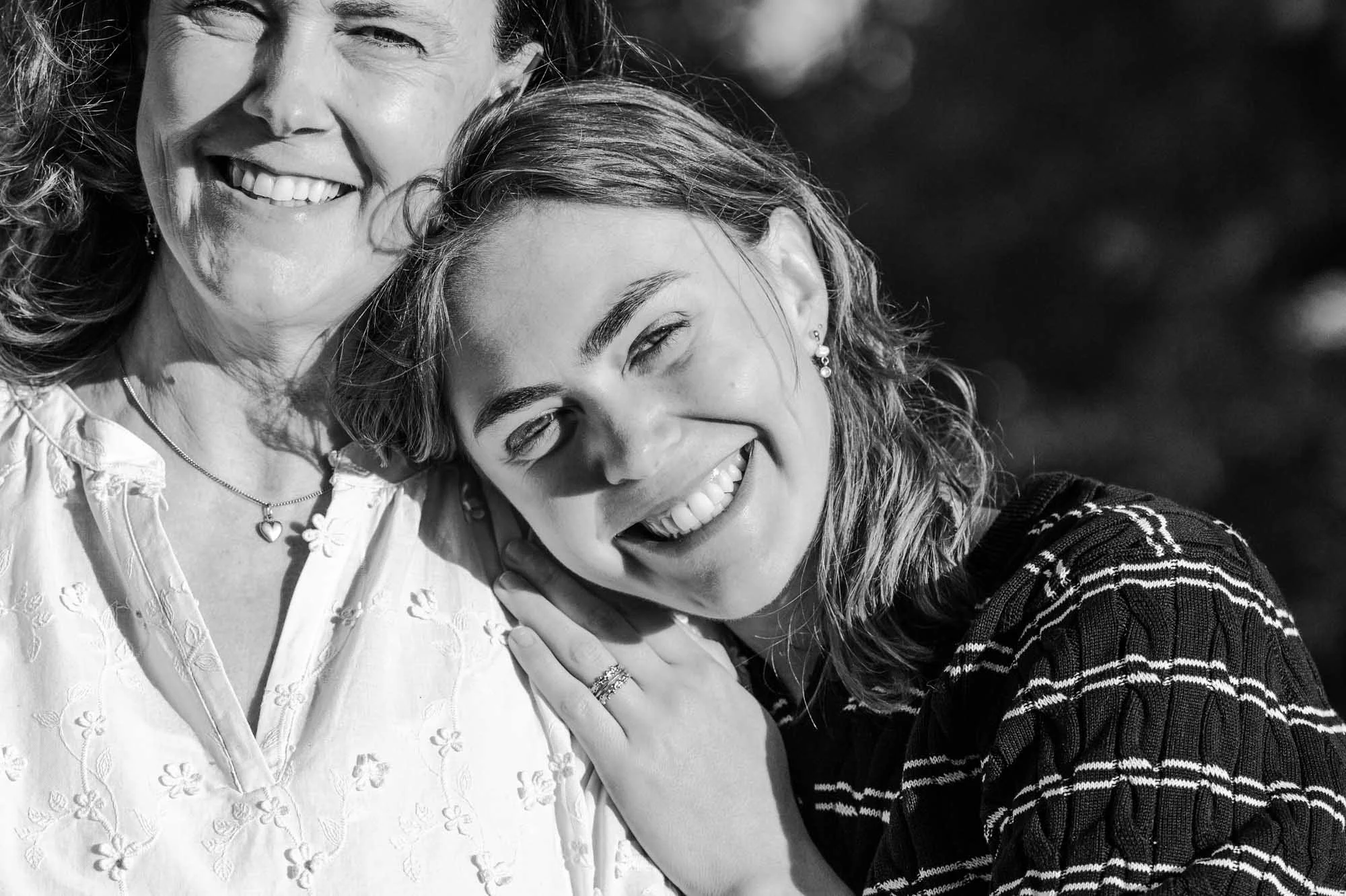 "Zwart-wit close-up van Amber Sels die haar hoofd tegen haar mama leunt met een brede glimlach, lifestyle portret in natuurlijk daglicht"