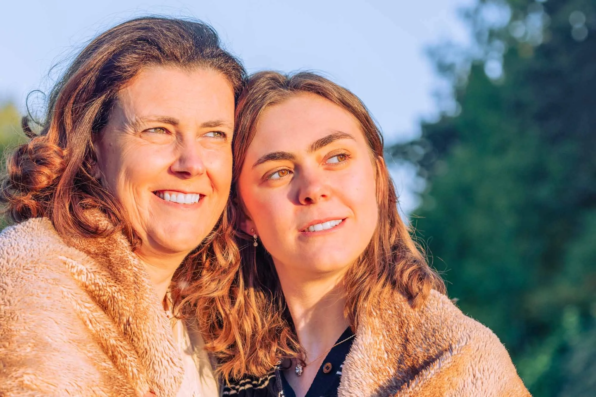 "Amber Sels en haar mama onder een zachte deken, samen kijkend naar de ondergaande zon – intiem moeder-dochterportret in warm licht"
