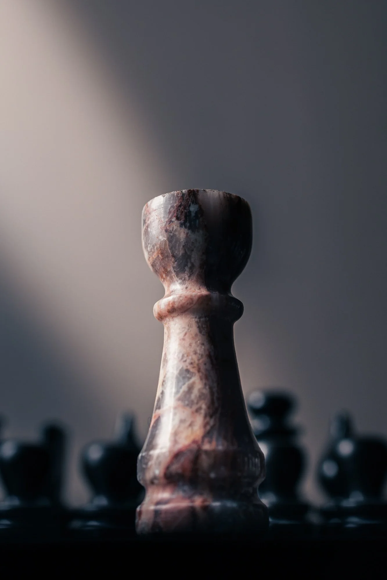 Close-up of a marble chess king piece on a chessboard with blurred chess pieces in the background.