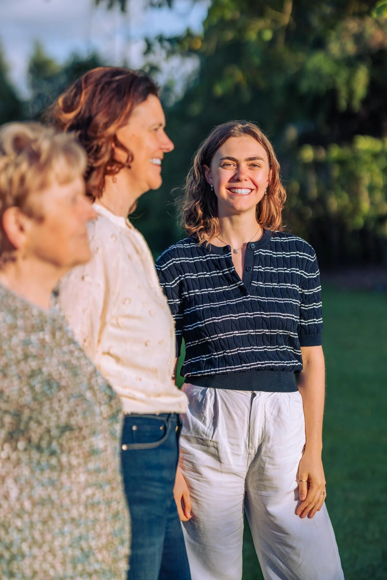 "Amber Sels poseert lachend in het avondlicht naast haar mama en grootmoeder tijdens een lifestyle familieportret in Rijmenam"
