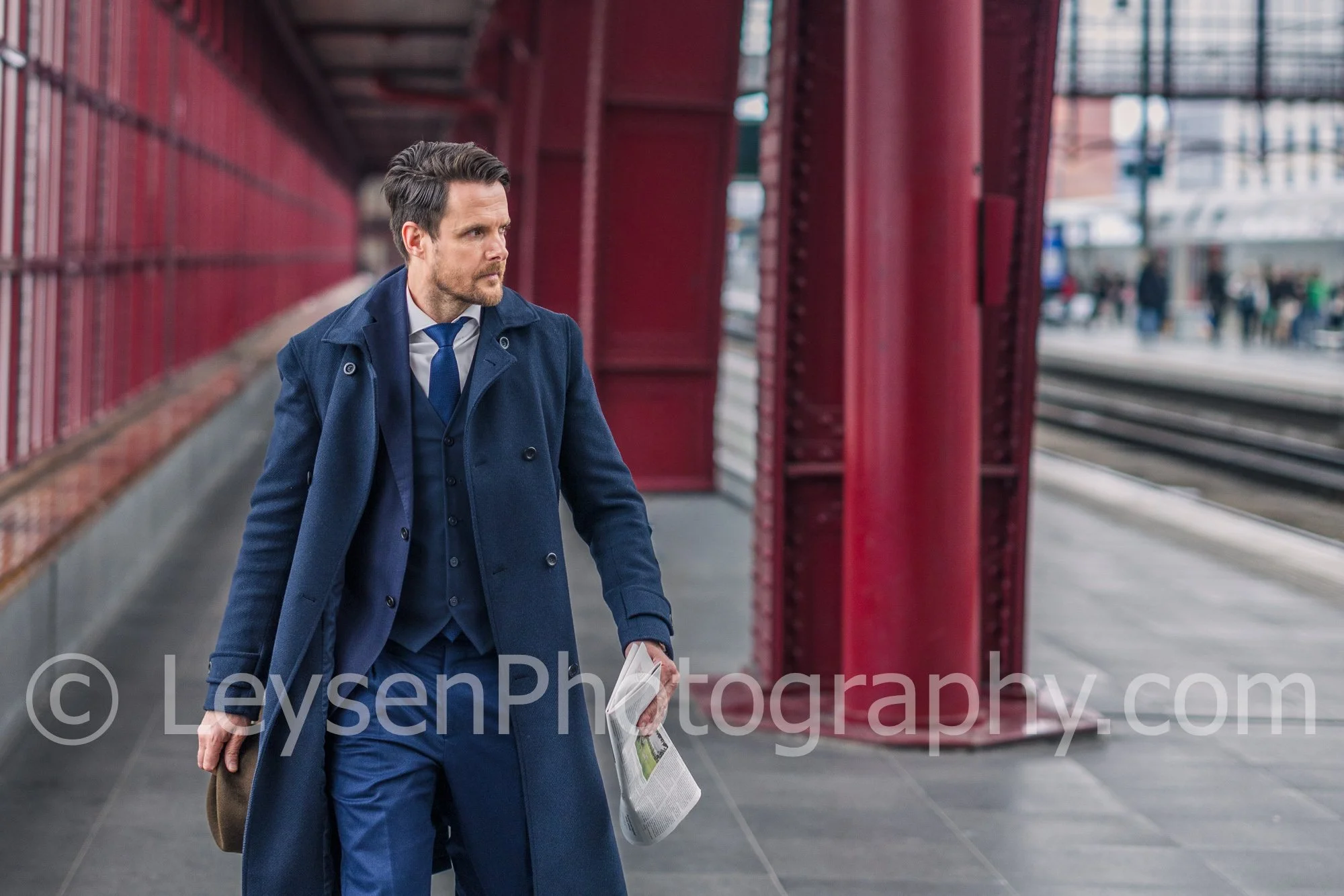Professional businessman walking along urban train station holding head and newspaper