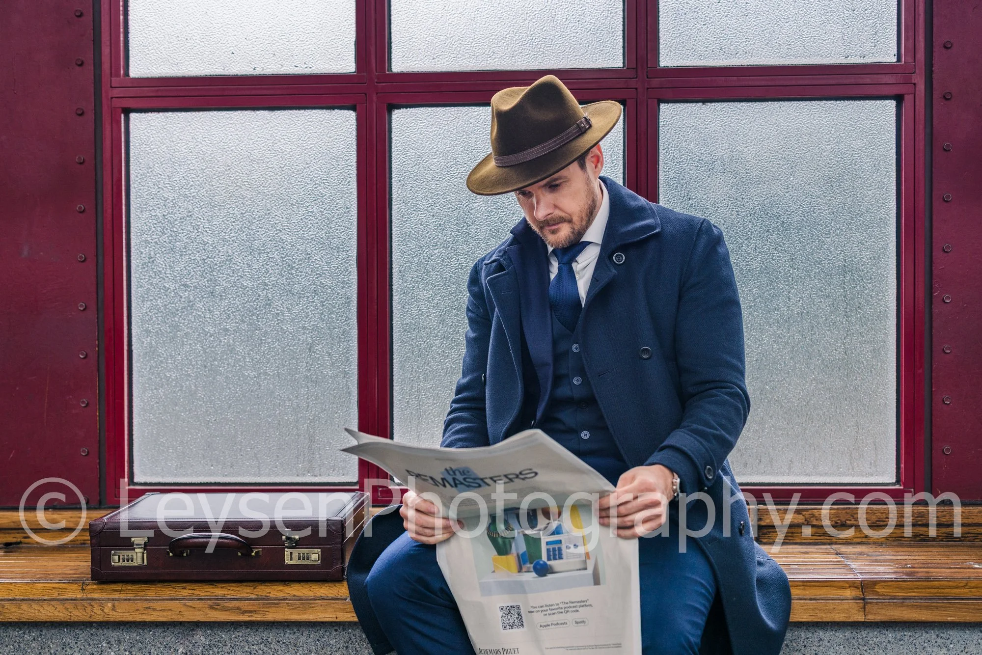 Elegant businessman wearing hat reading newspaper at station