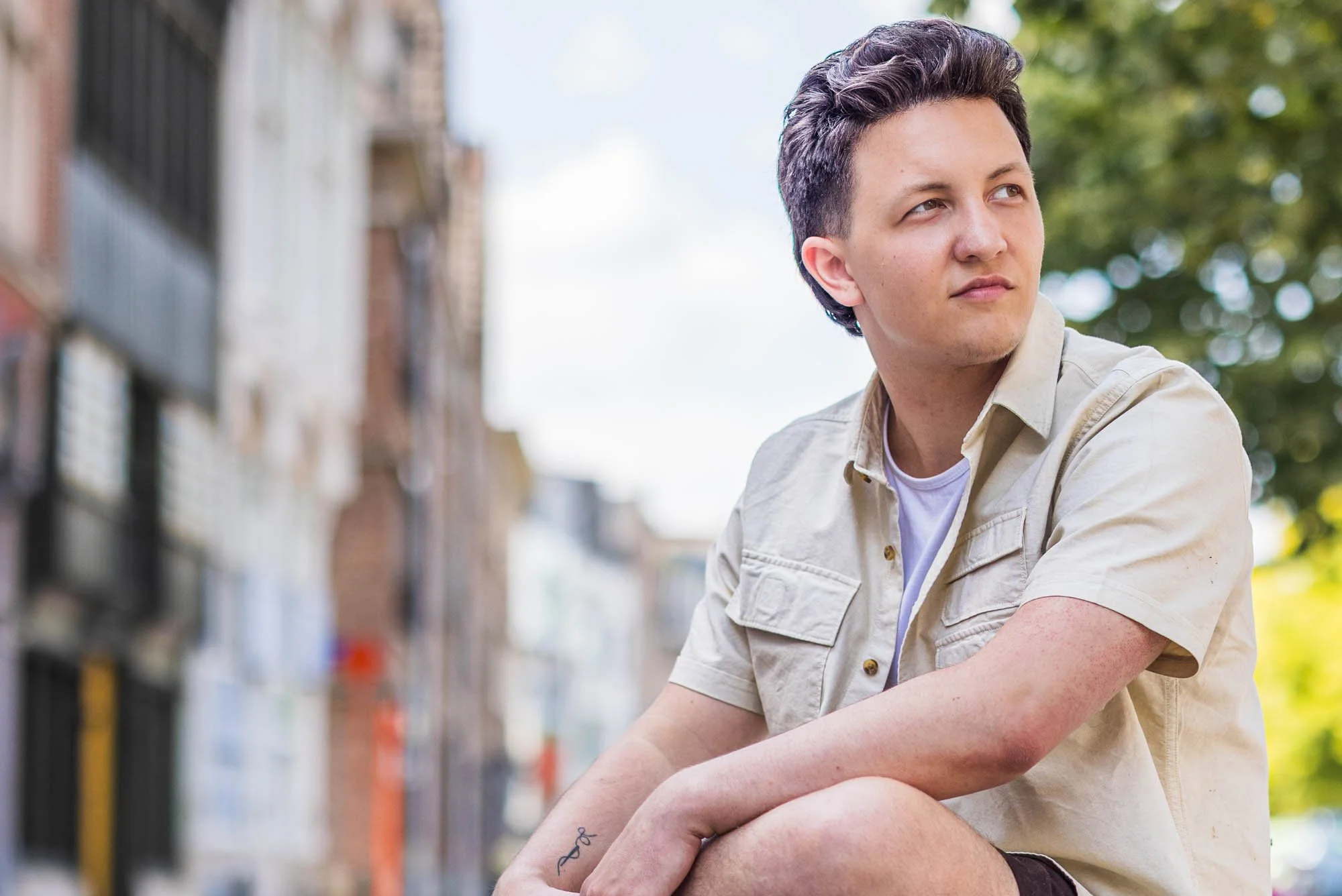 Portret van Alex Verspecht zittend op een stoep met een bedachtzame blik, straatbeeld van Mechelen op de achtergrond"
