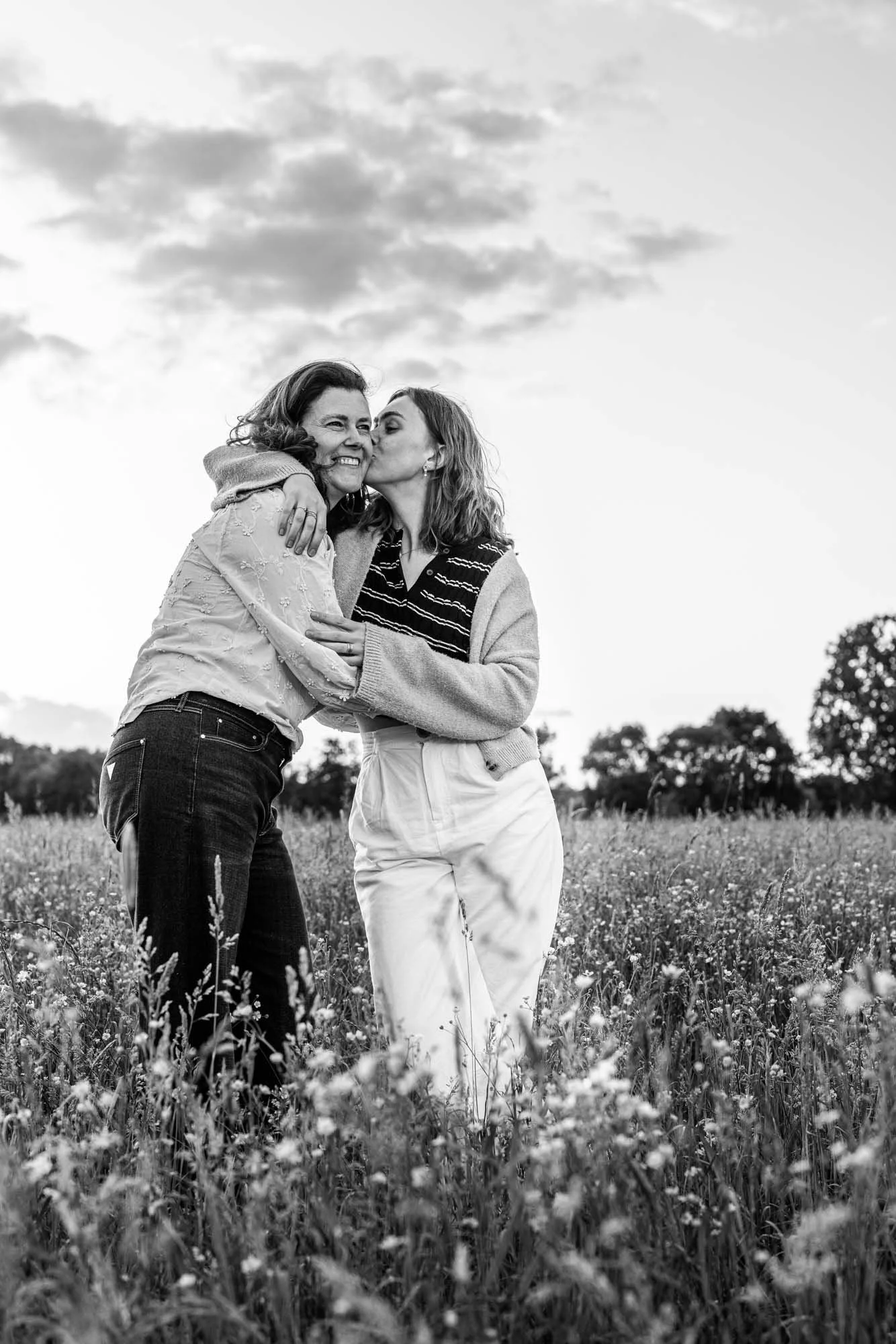 Spontaan moment tussen moeder en dochter in zwart-wit. Intieme familieportretfoto door Leysen Photography in een natuurlijk veld bij valavond.