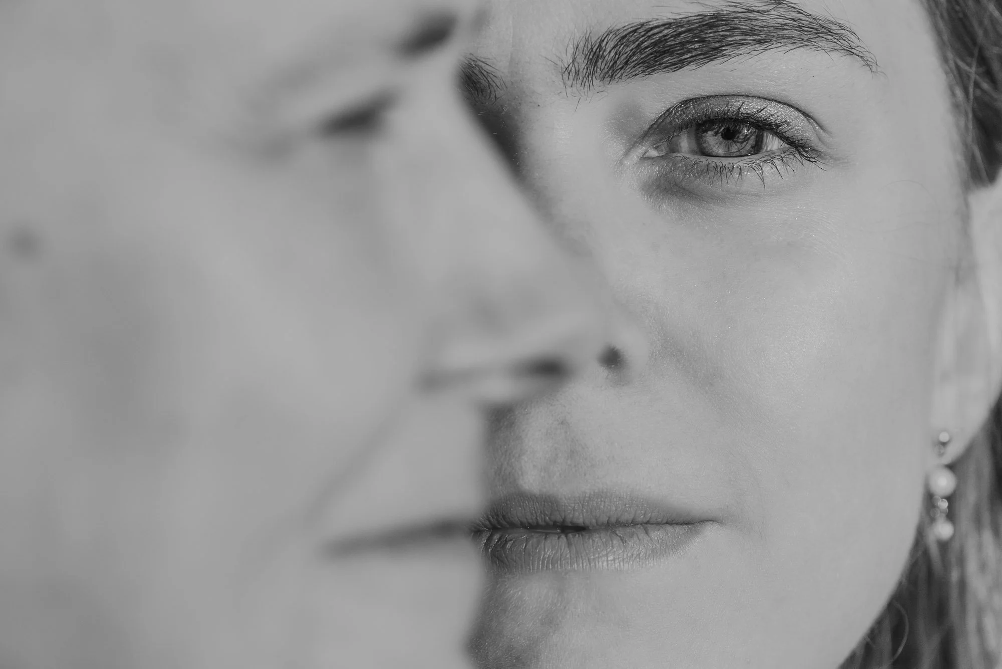 Zwart-wit detailopname van Amber Sels’ gezicht scherp in beeld, met het gezicht van haar mama onscherp op de voorgrond – intiem moeder-dochter portret