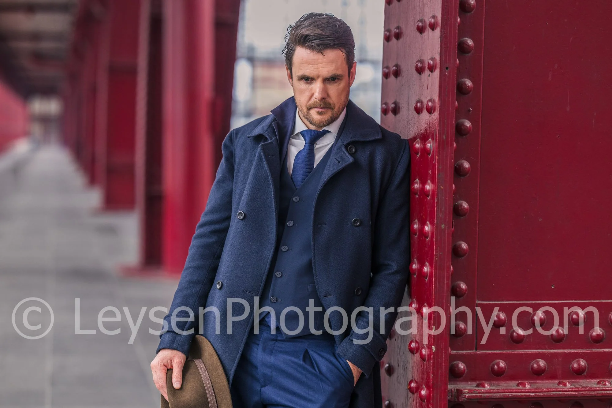 Stylish Businessman Holding Hat Next to Red Architectural Column