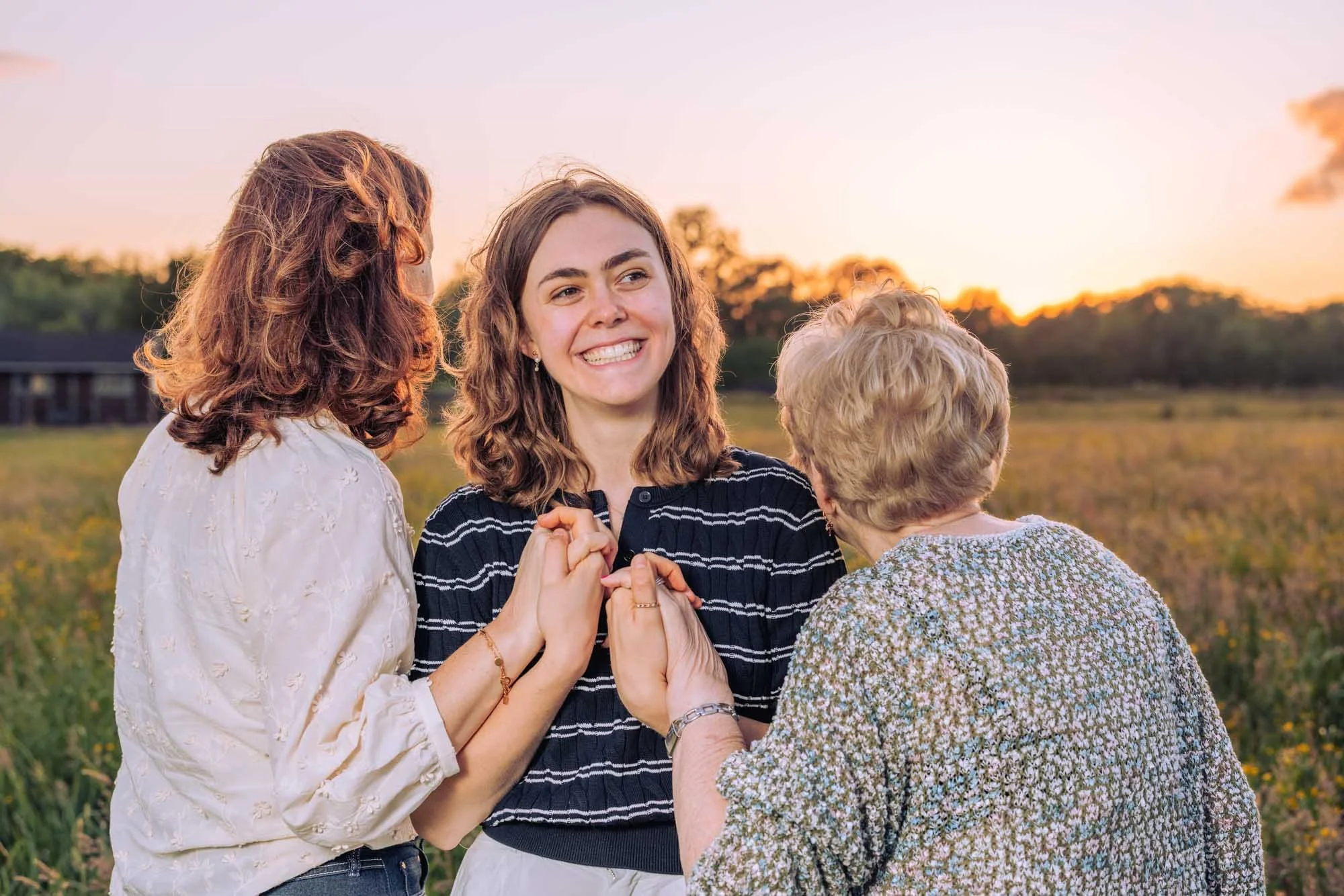 Drie vrouwen hand in hand in een veld bij zonsondergang
Moeder, dochter en grootmoeder houden elkaars handen vast tijdens een intiem moment in een bloemenveld. Familieportret door Leysen Photography met gouden licht.