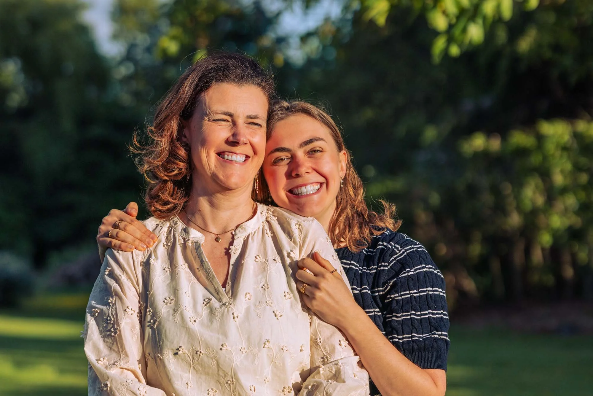 "Portret van Amber Sels die liefdevol haar mama omhelst in een zomerse tuin in Rijmenam, beiden stralend lachend naar de camera"
