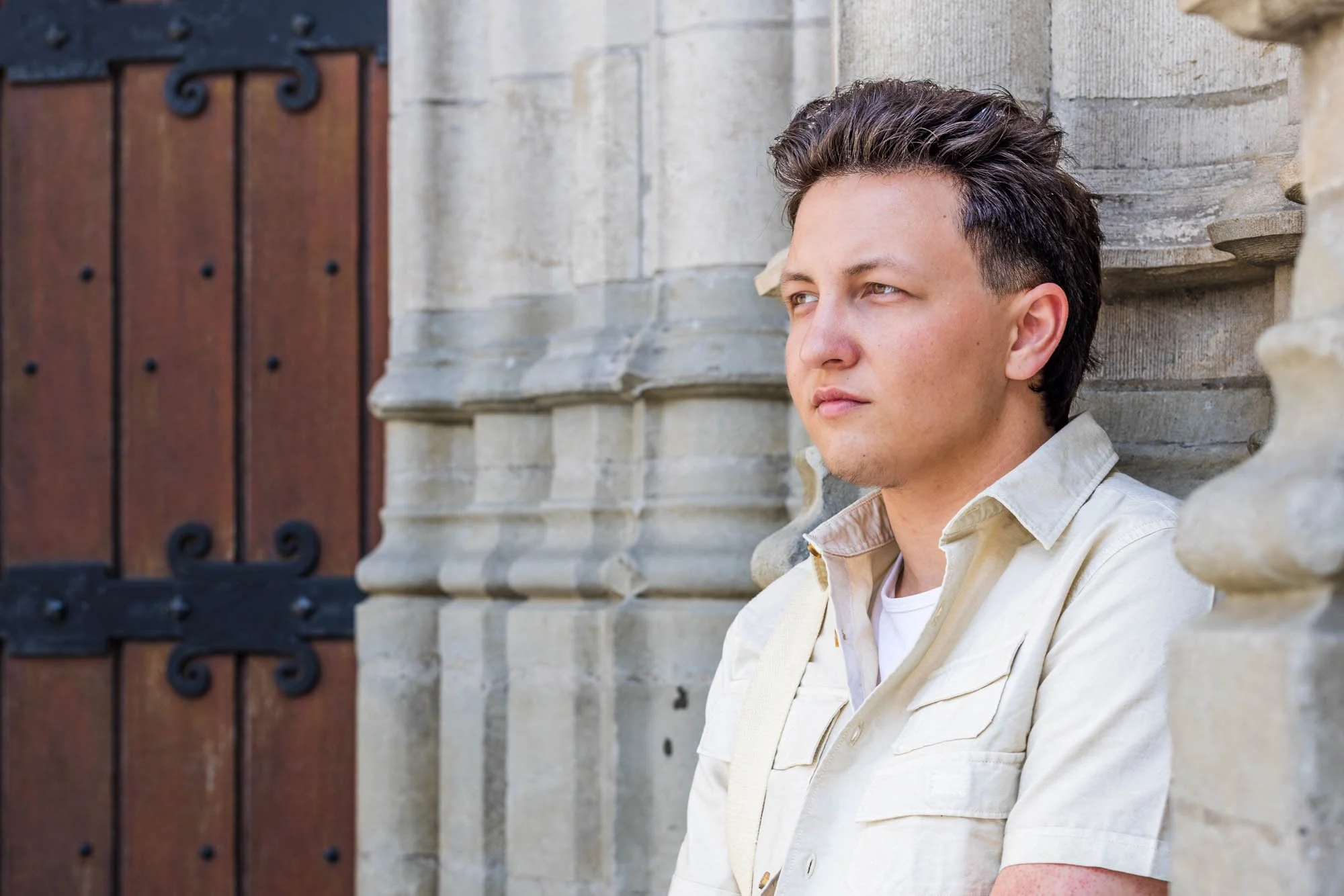 Expressief portret van Alex Verspecht voor een oude kerkgevel met stenen zuilen, gefotografeerd in historisch Mechelen" locatie: sint Rombouts toren