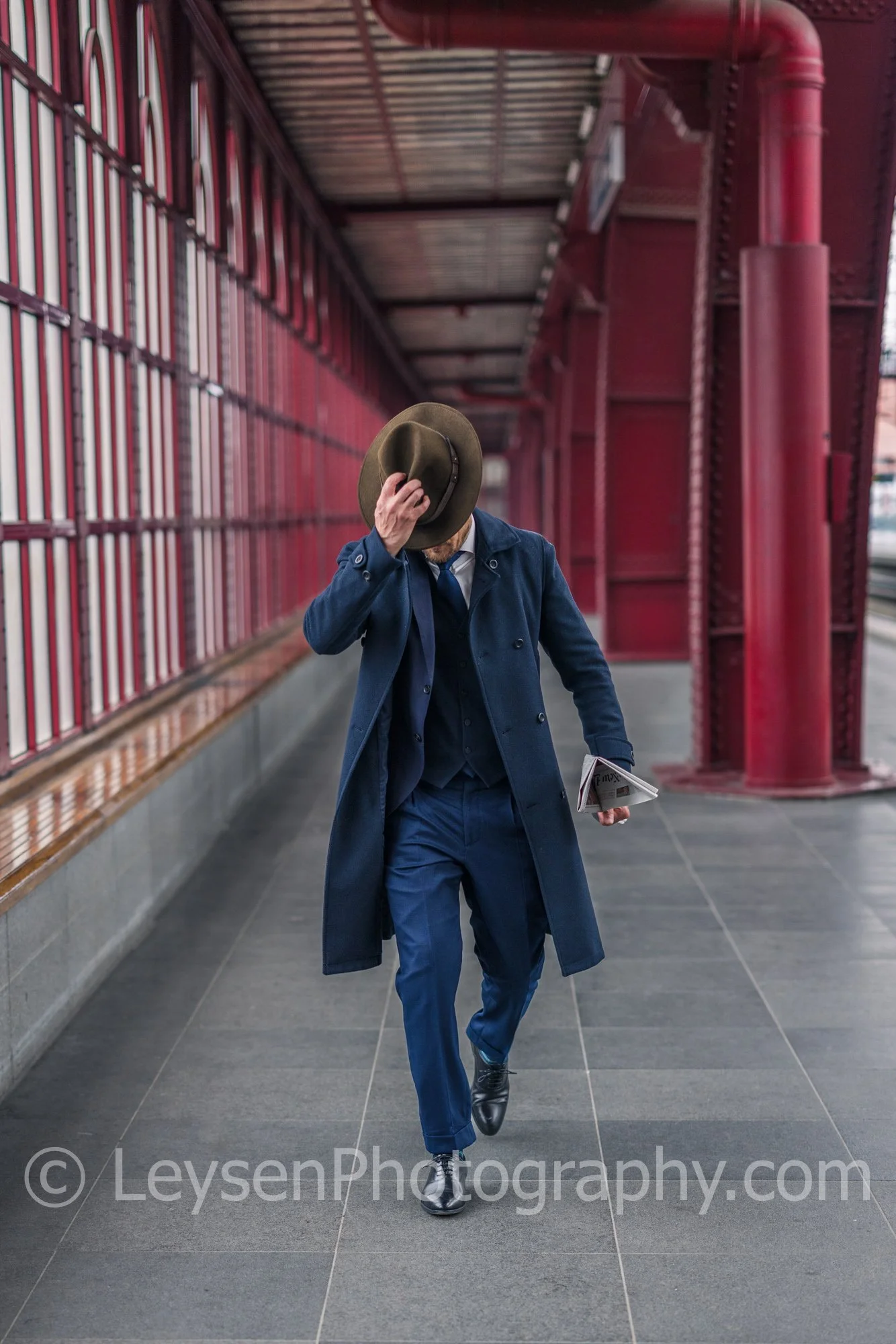 Businessman walking with hat and newspaper at train station