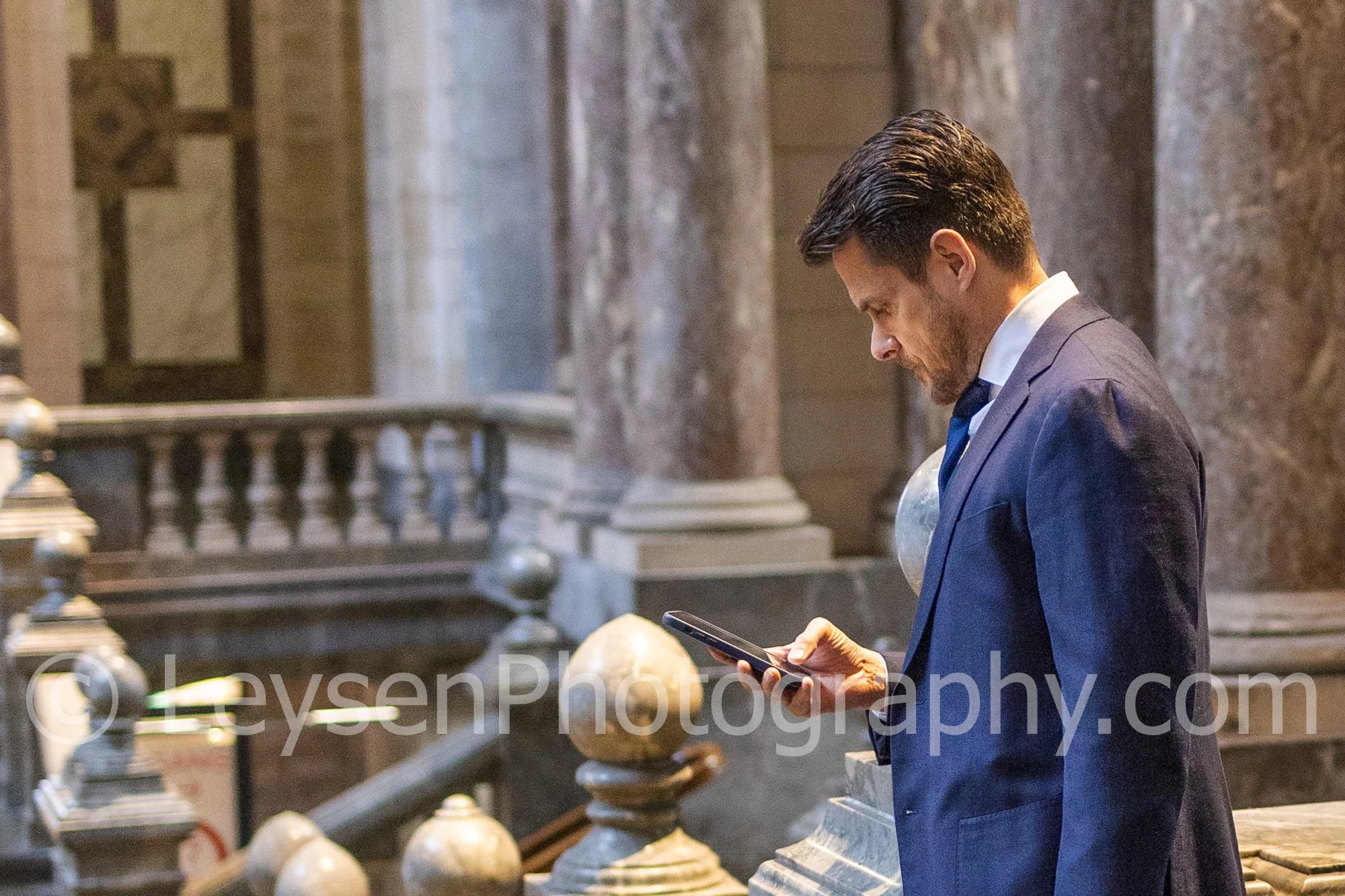 Professional businessman looking at smartphone near marble staircase