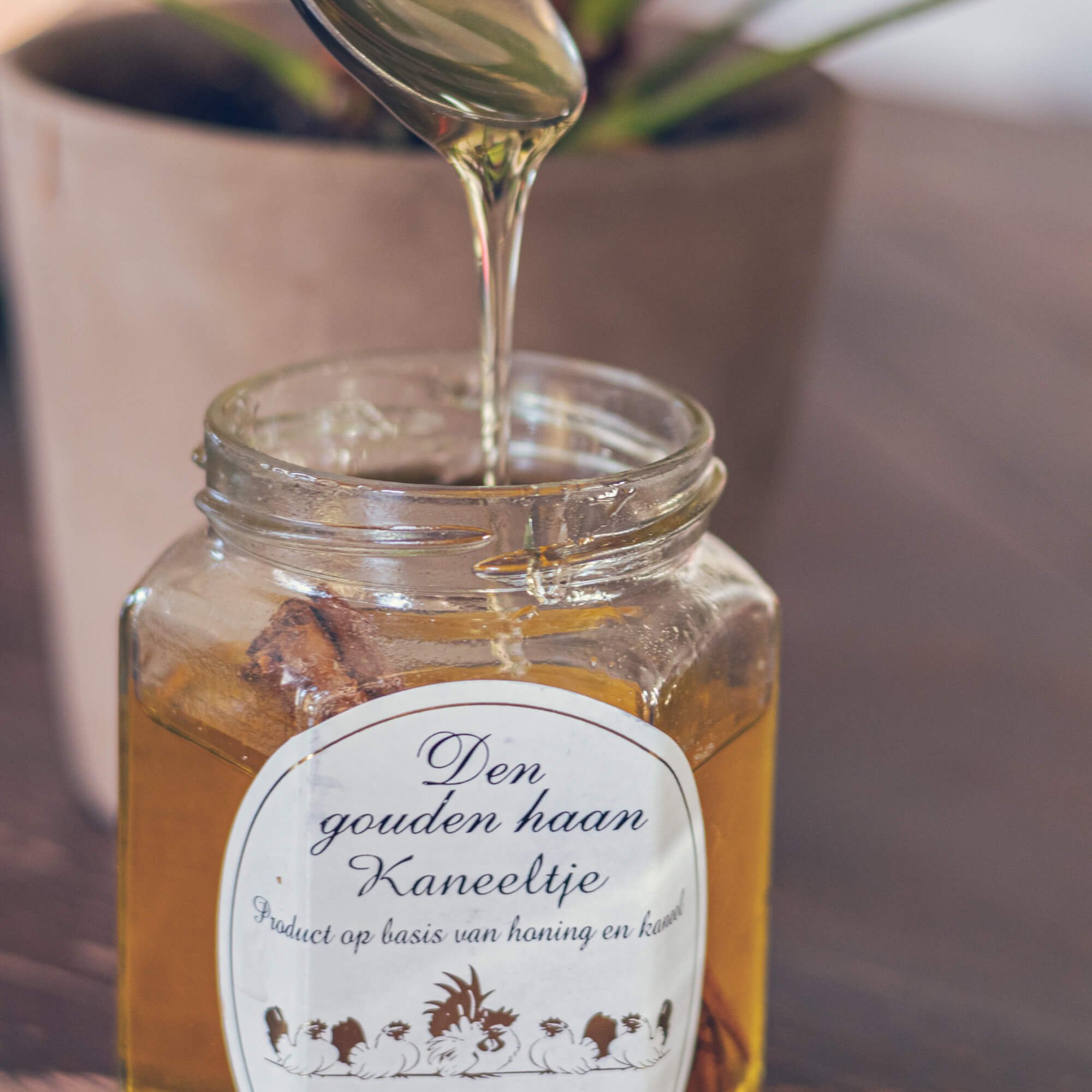 Honey being poured from a spoon into a glass jar labeled in Dutch, with duck illustrations on the label.
