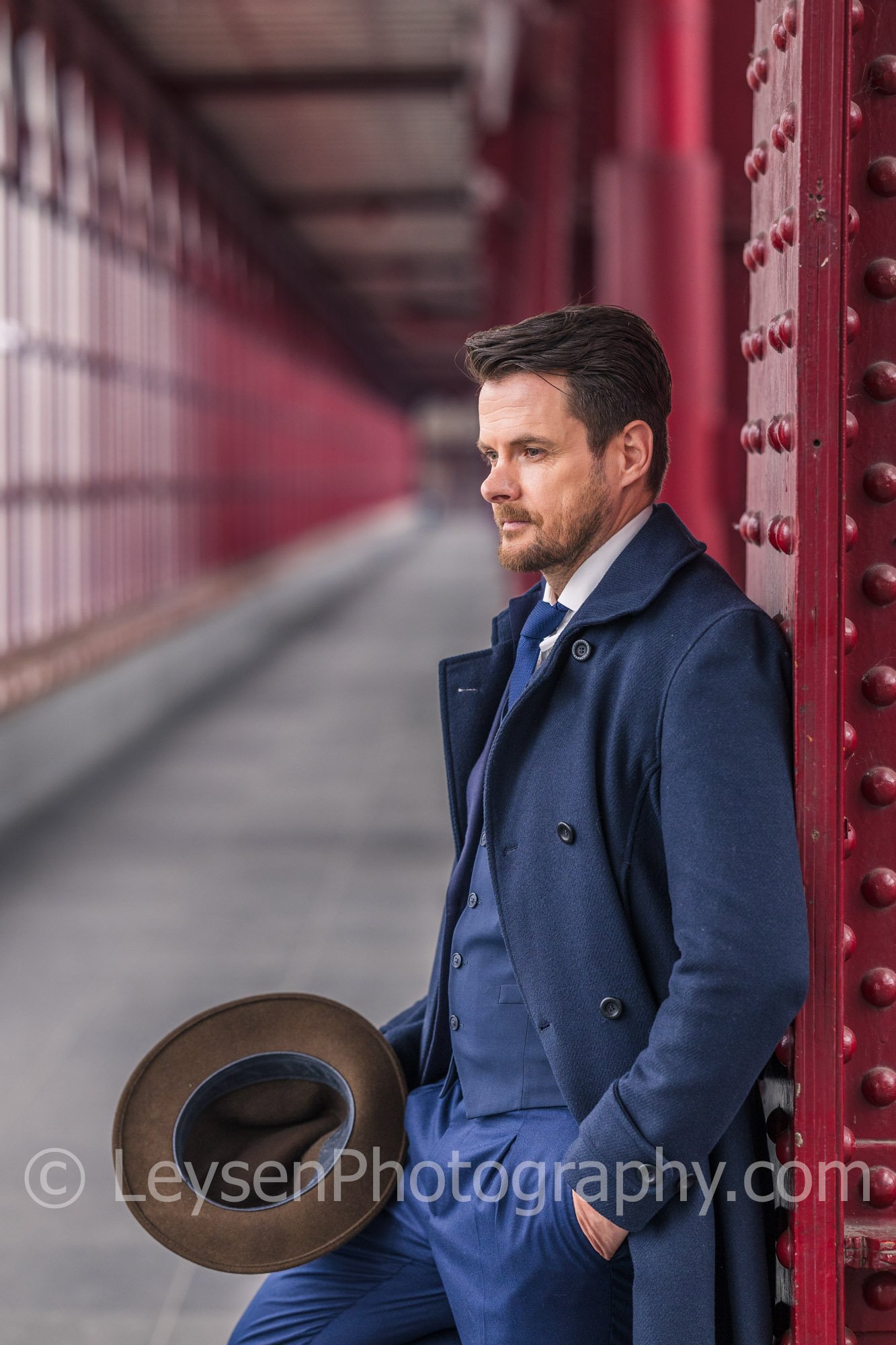 Professional Businessman Leaning Against Red Steel Column Holding Hat