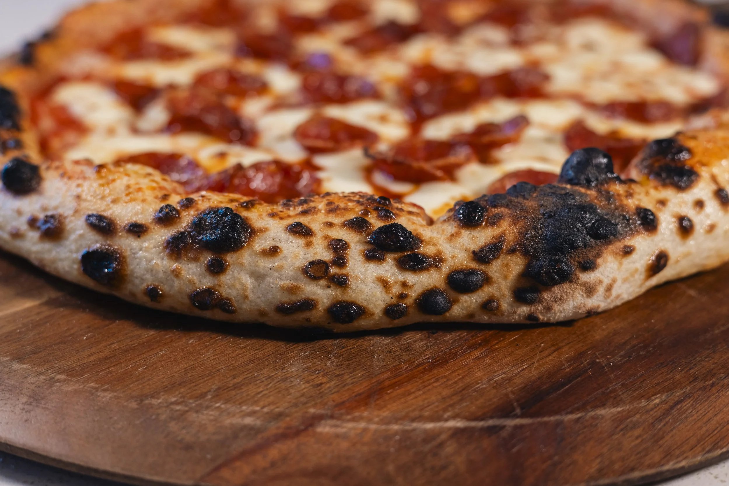 Close-up of a pepperoni pizza with a charred crust on a wooden surface.