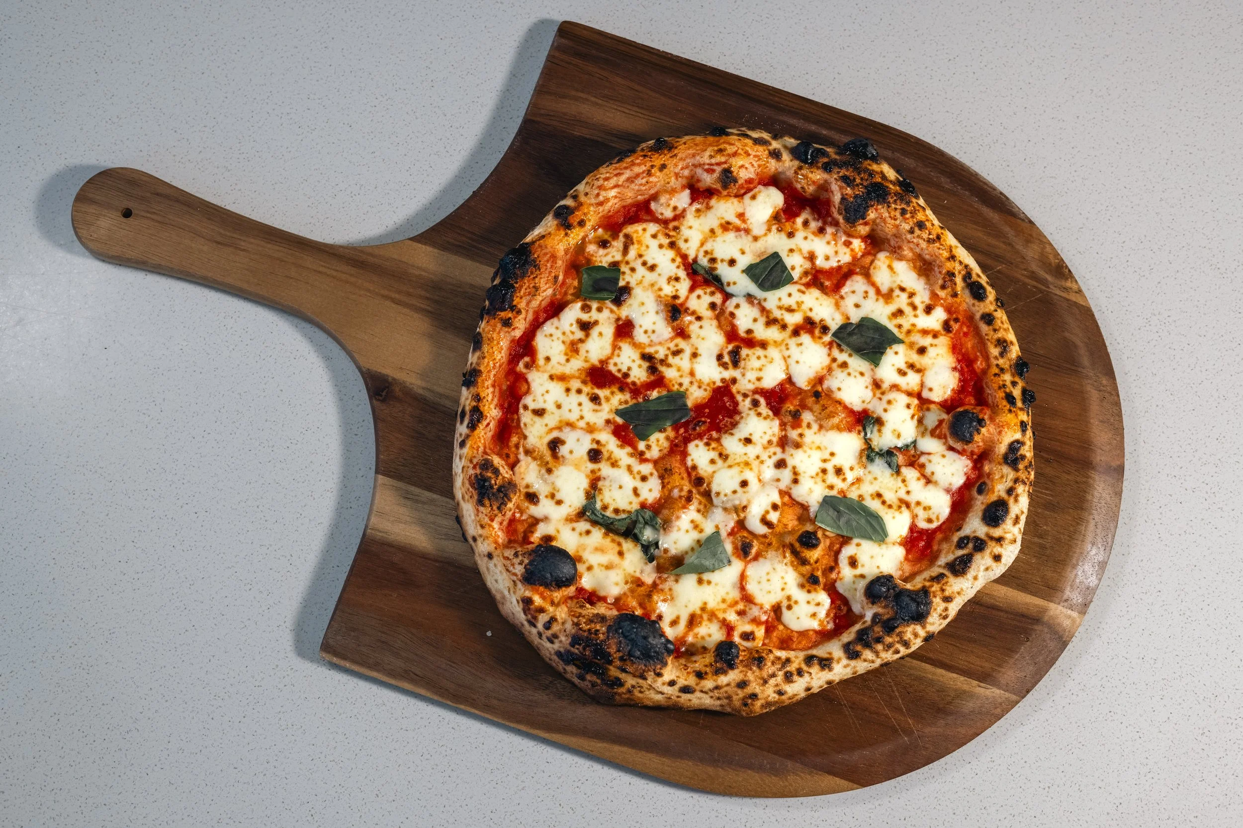 A freshly baked pizza with cheese, basil, and tomato sauce on a wooden serving board.