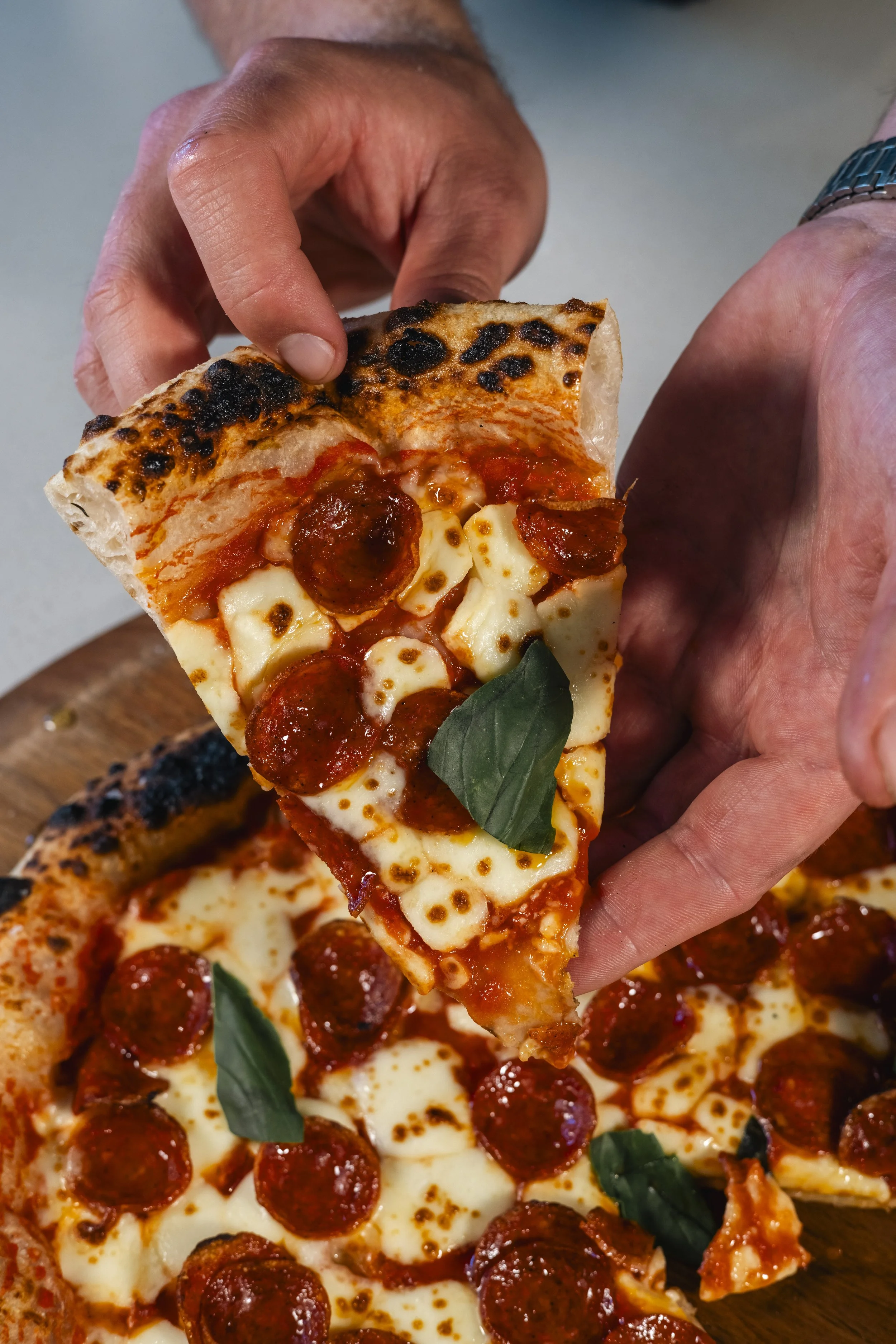 A person holding a slice of pepperoni pizza with melted cheese and fresh basil leaves.