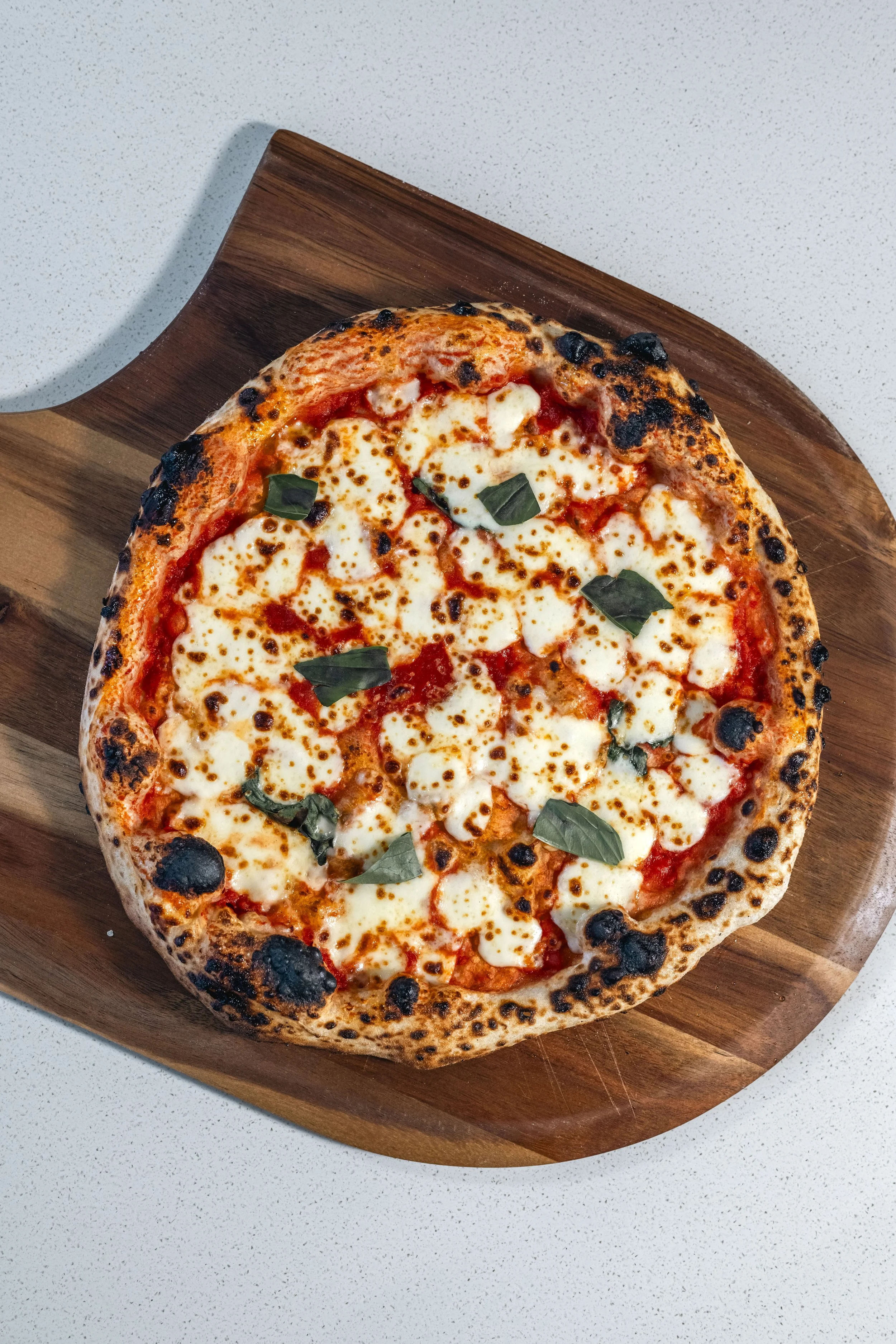 A cheese pizza with basil leaves on top, placed on a wooden serving board.