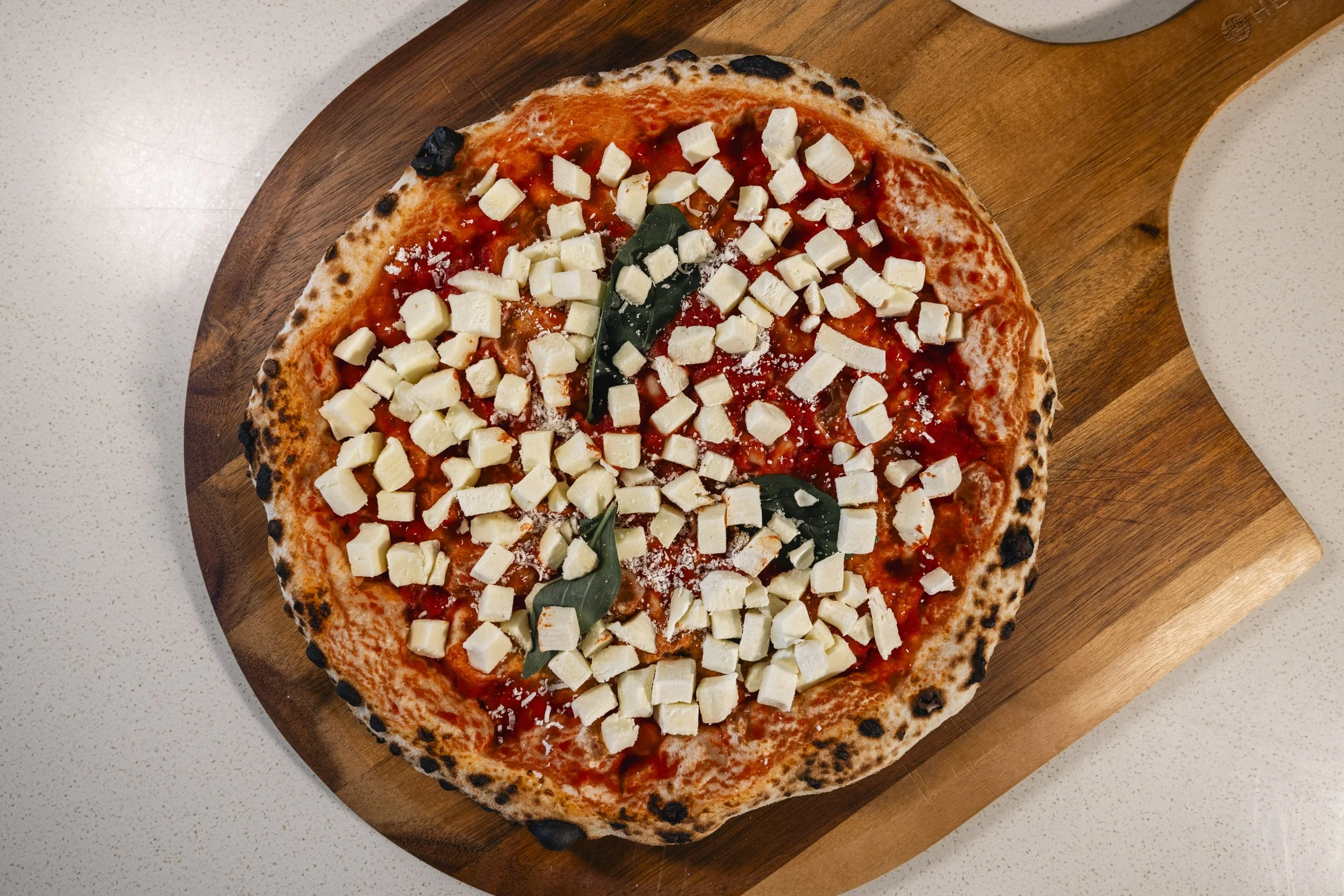 A cheese pizza with a thin crust, topped with mozzarella cheese, basil leaves, and tomato sauce, served on a wooden pizza paddle.
