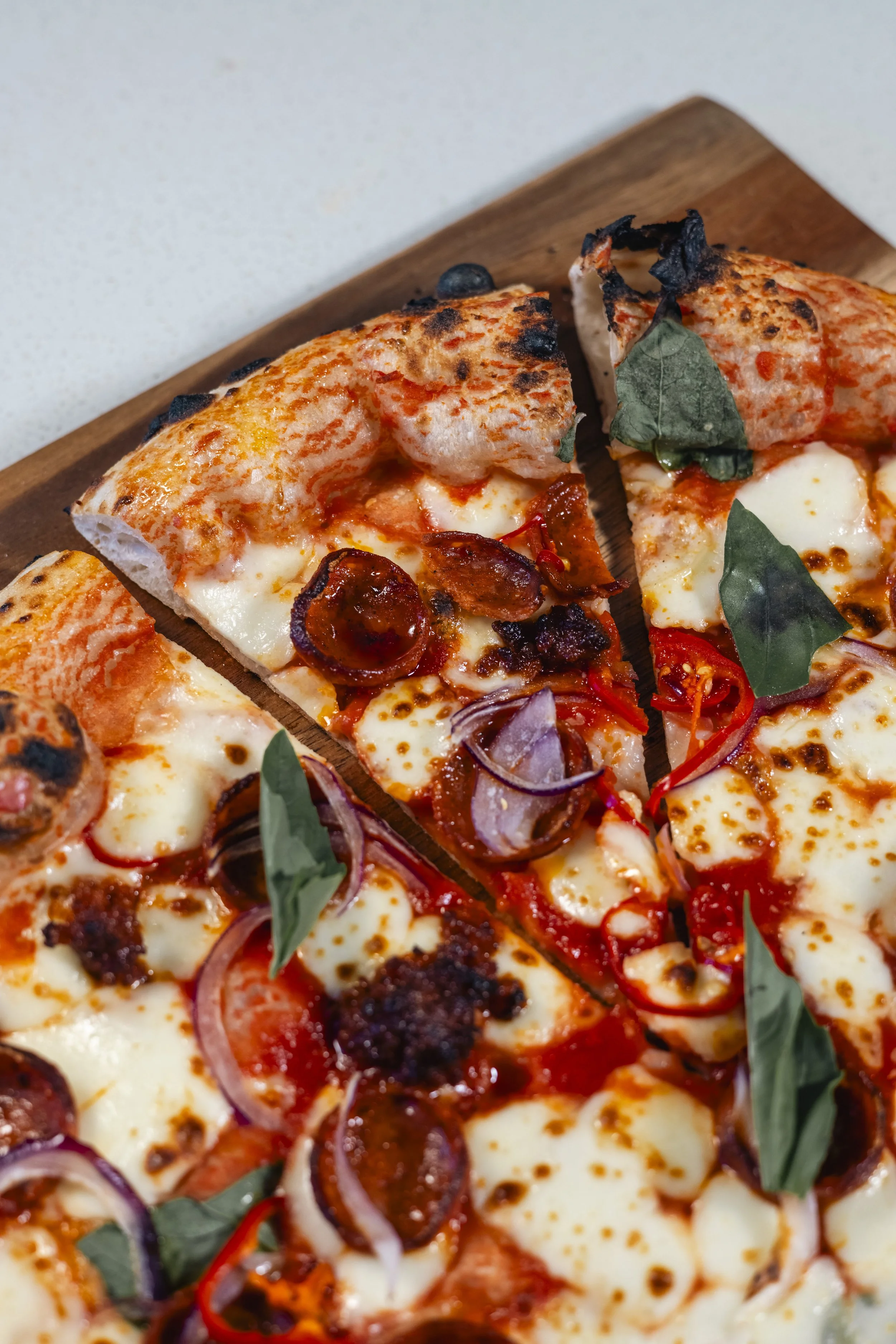 Close-up of a variety of pizza slices on a wooden surface, topped with cheese, pepperoni, red onions, and fresh basil leaves.