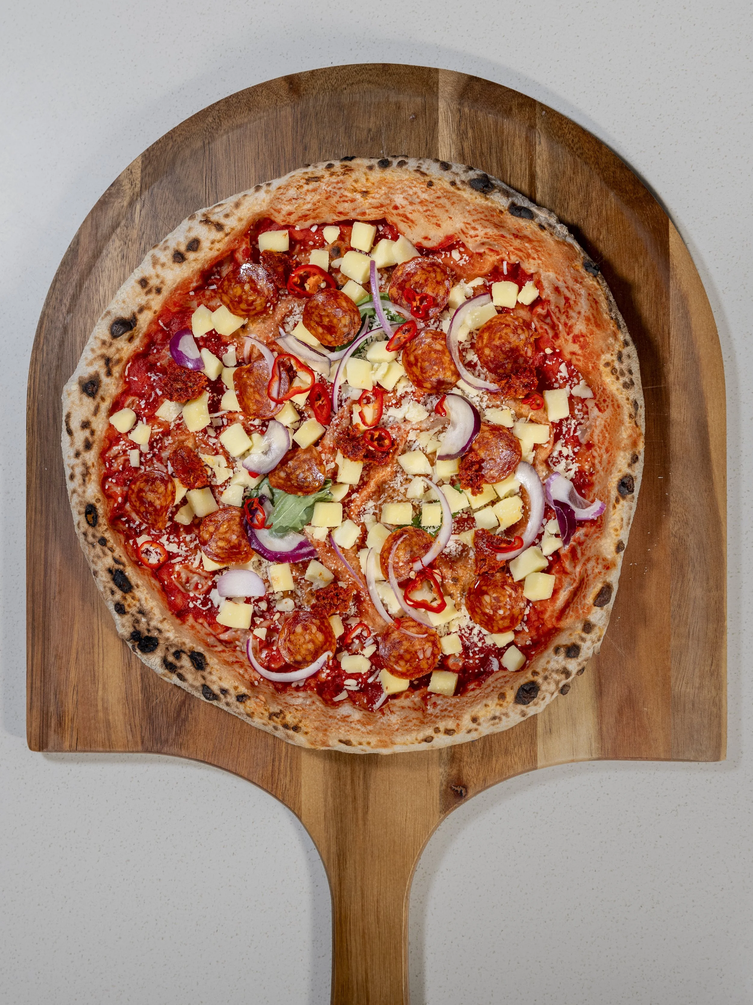 A partially eaten pizza with toppings including meatballs, sliced red chili peppers, onions, pineapple chunks, and cheese on a round wooden pizza board.