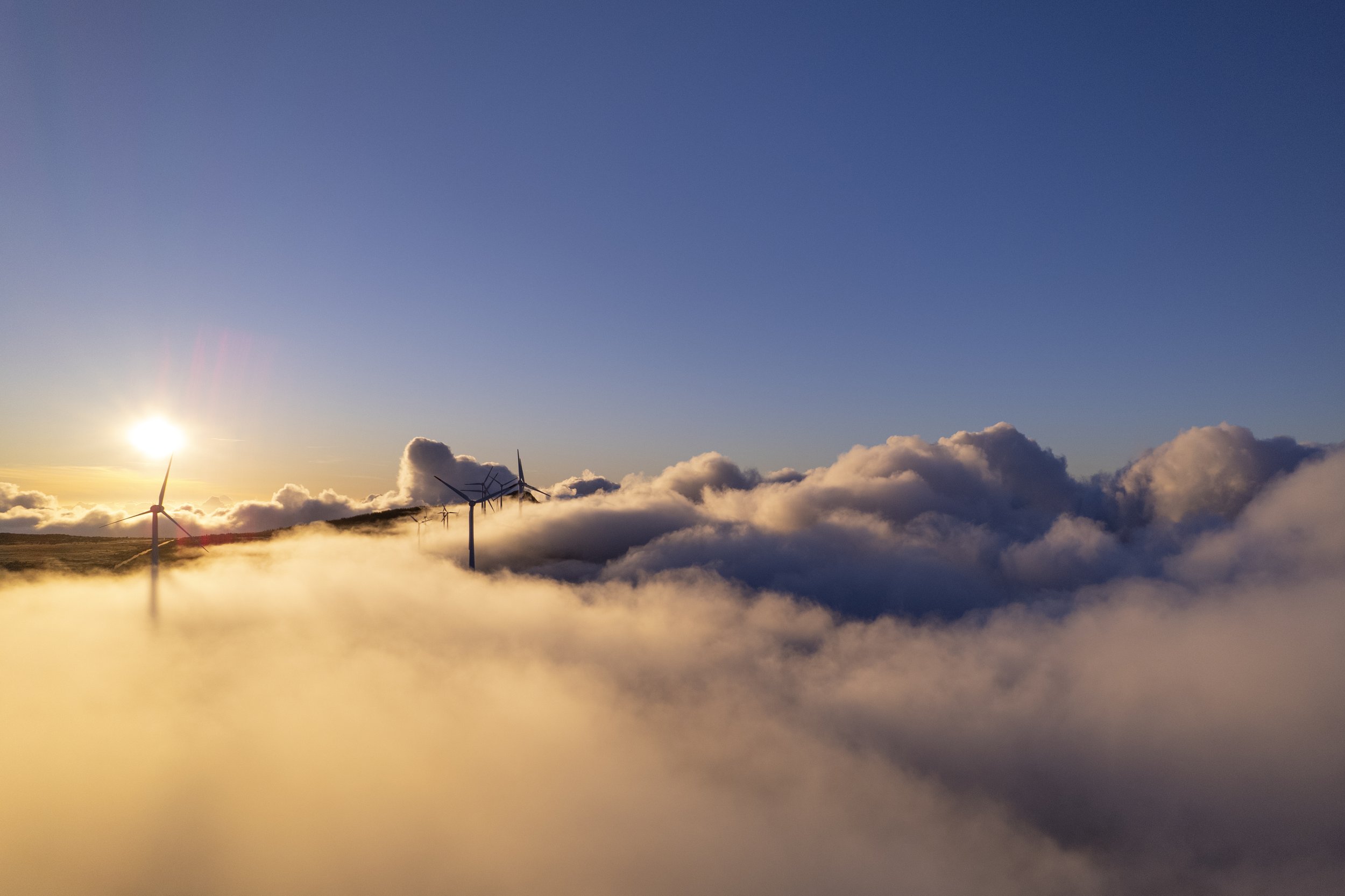 A scenic view of wind turbines on a hilltop surrounded by clouds during sunset or sunrise.
