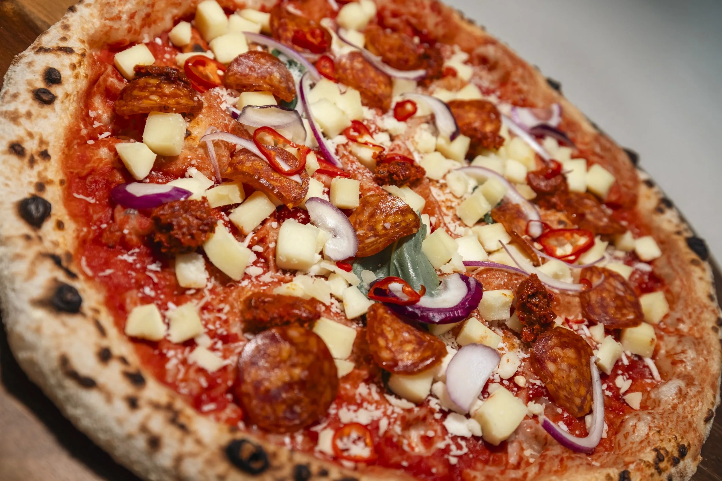 Close-up of a pepperoni pizza with cheese, red onions, sliced red chili peppers, and sausage on a thin crust.